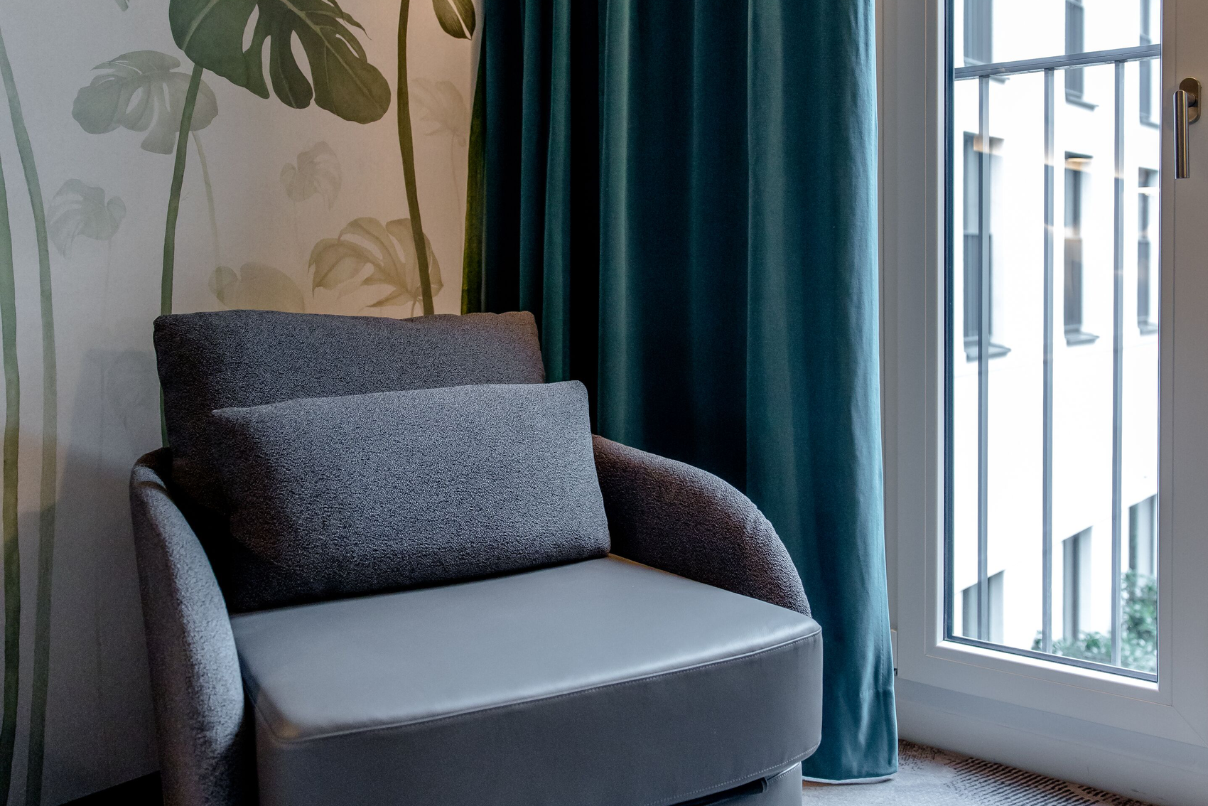 designhotel Munich Hauptbahnhof Motel One room with gray armchair in front of floor-to-ceiling window
