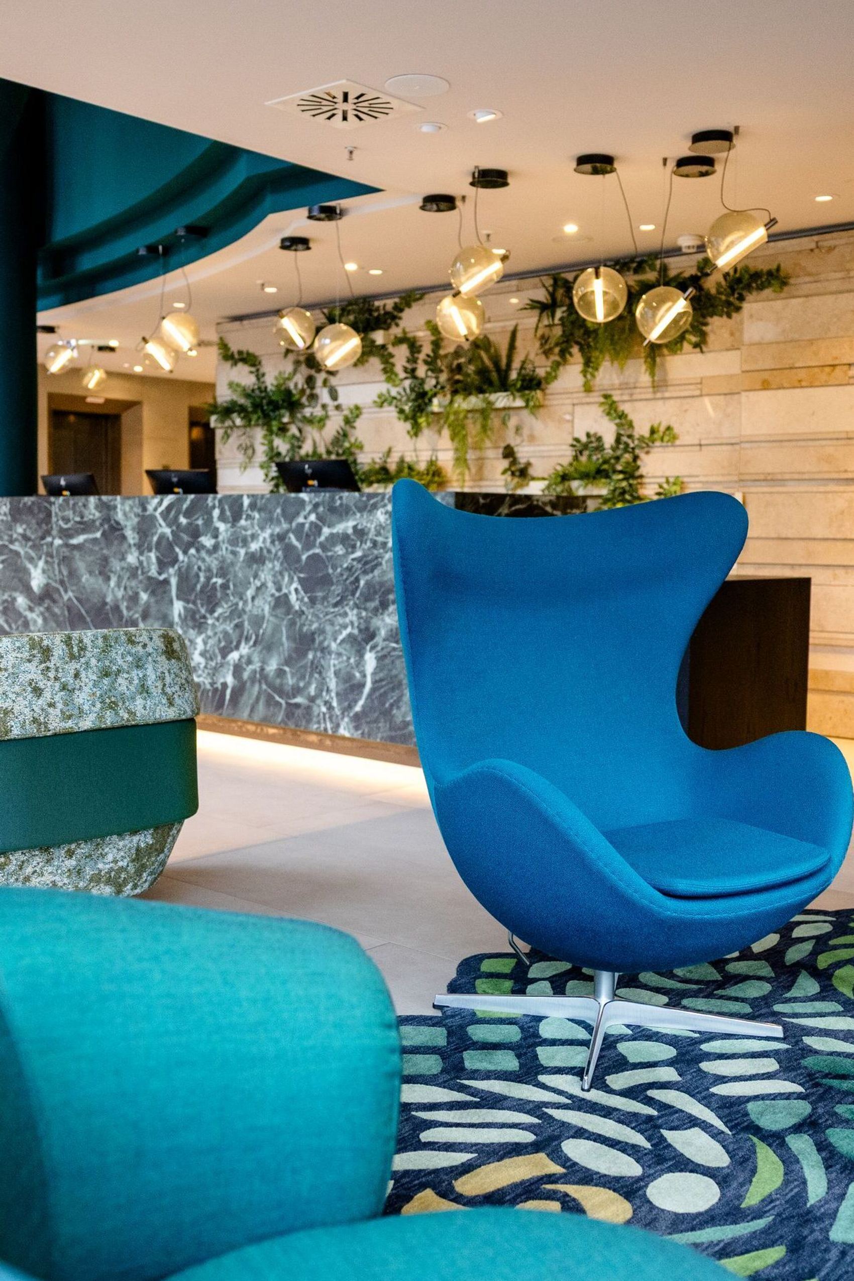 Hotel Frankfurt-Hauptbahnhof Motel One Lounge mit stilvollen, komfortablen Sesseln in Blau- und Türkistönen, kreativer Beleuchtung und grünen Pflanzen.