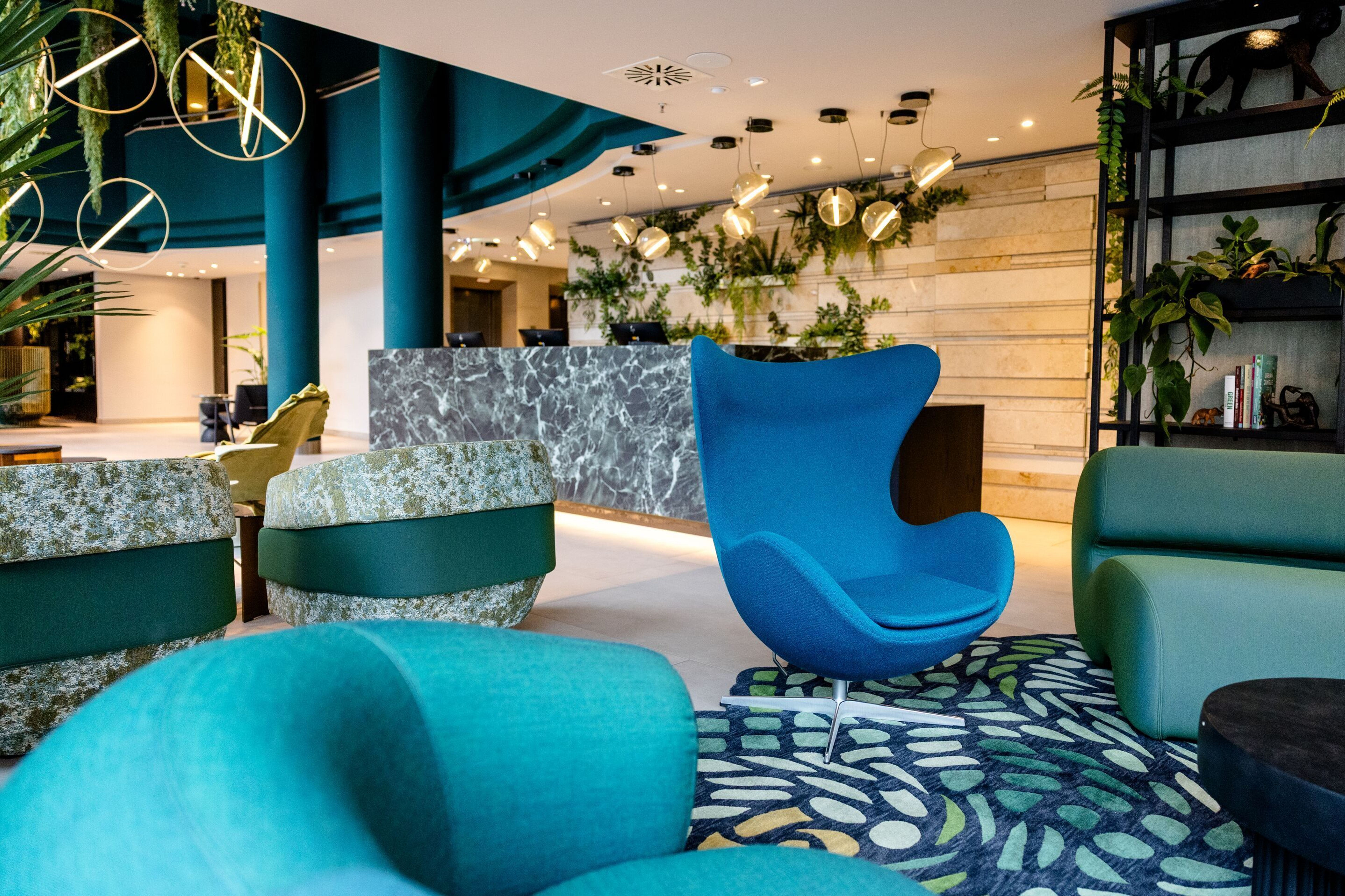 Hotel Frankfurt-Hauptbahnhof Motel One Lounge mit stilvollen, komfortablen Sesseln in Blau- und Türkistönen, kreativer Beleuchtung und grünen Pflanzen.
