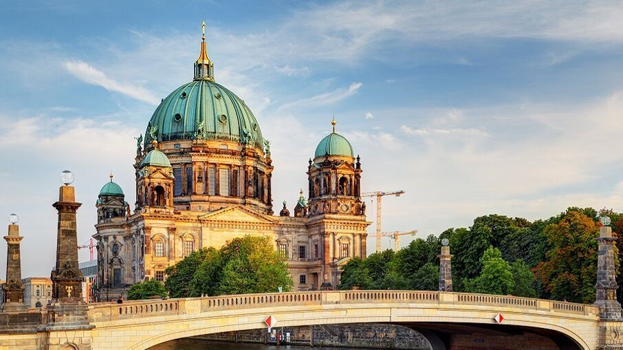 Blick auf den Berliner Dom mit seiner historischen Kuppel und angrenzender Brücke über die Spree, umgeben von Grün und einem klaren Himmel im Abendlicht. Ideal für kulturell interessierte Reisende.