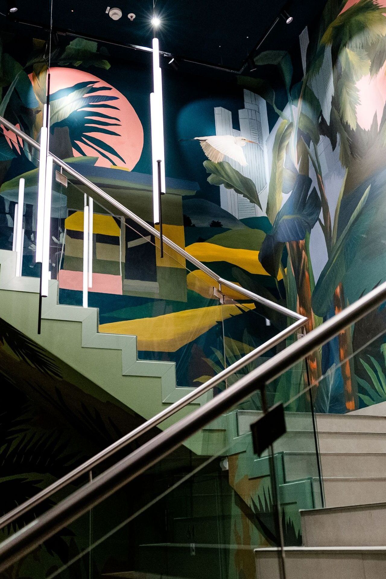 Bunte Wendeltreppe mit tropischen Wandgemälden in lebendigen Farben, die eine entspannte, exotische Atmosphäre schaffen. Edelstahl-Geländer reflektieren das Licht, das die Szenen sanft beleuchtet.