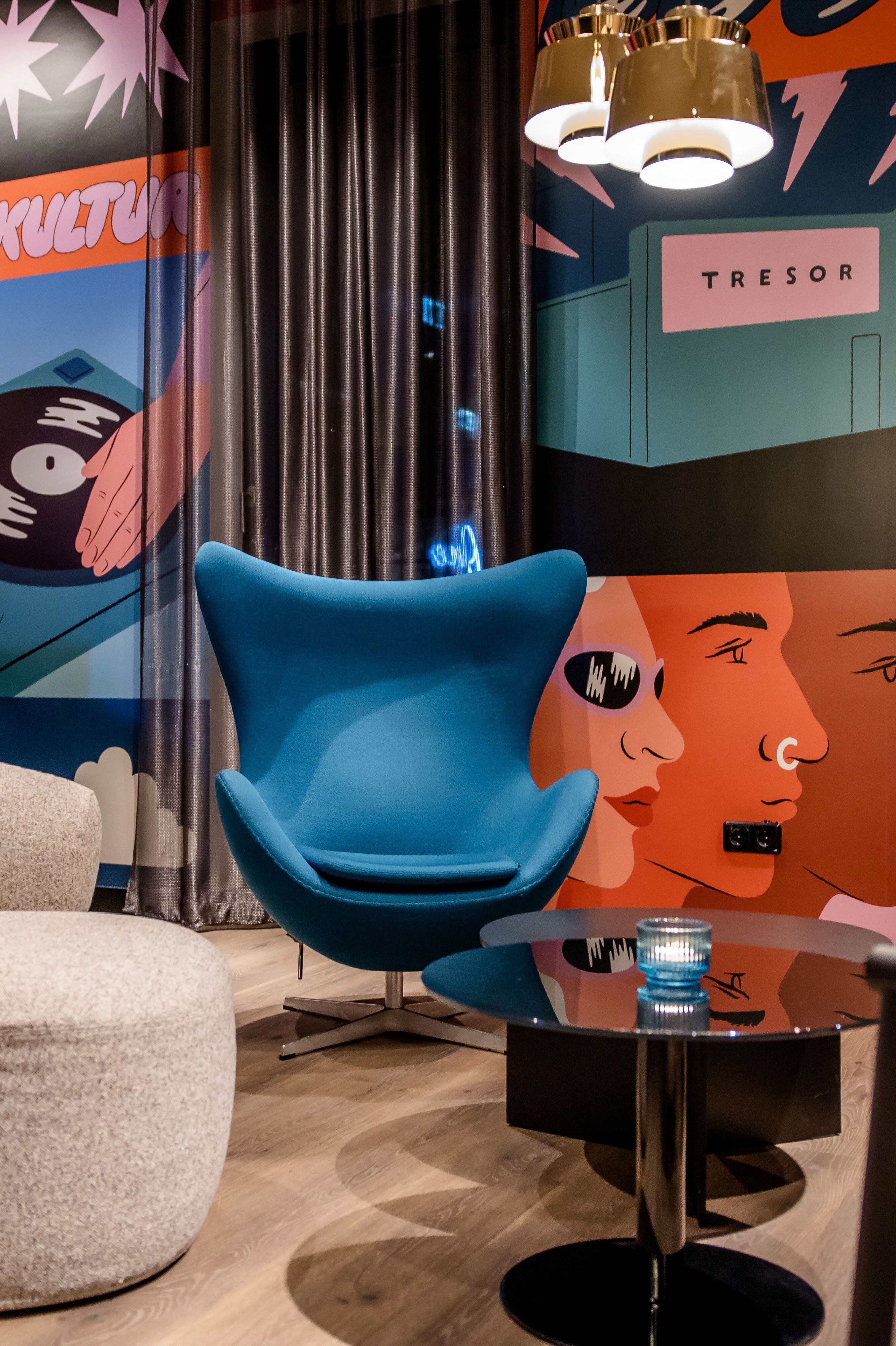 Hotel Berlin-Potsdamer Platz Motel One Lounge with colourful murals in retro techno style, comfortable armchairs and sofas, warm lighting and a round glass table, ideal for relaxing moments and creative encounters.