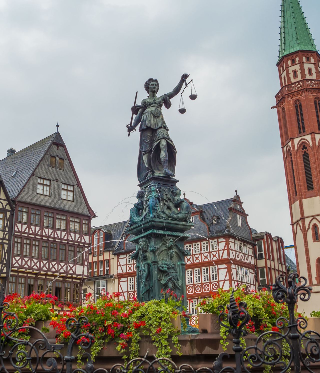 Marktplatz mit Fachwerkhäusern und der Statue der Justitia im Vordergrund, daneben ein hoher Kirchturm mit grünem Dach, an einem klaren Tag. Marktplatz mit Fachwerkhäusern und der Statue der Justitia im Vordergrund, daneben ein hoher Kirchturm mit grünem Dach, an einem klaren Tag.