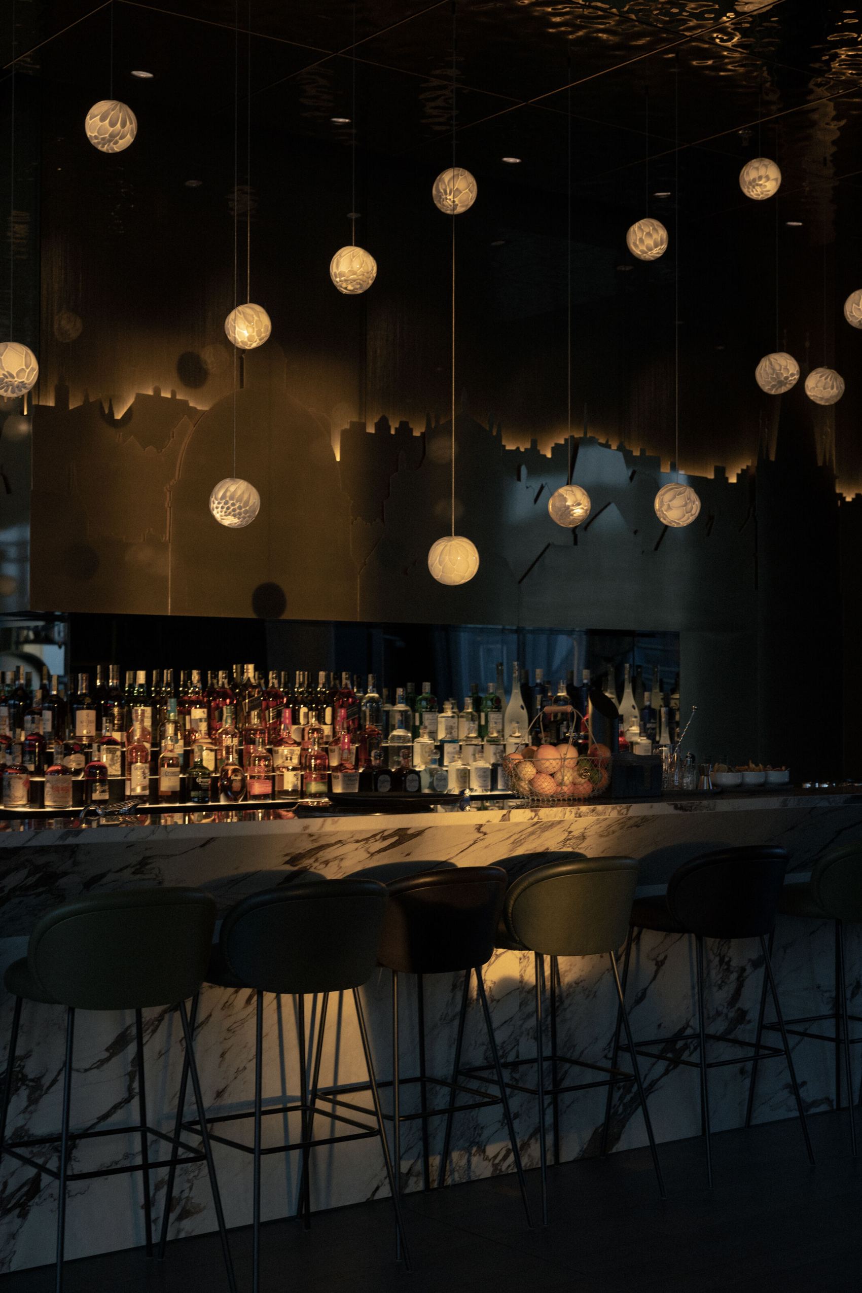 Hotelbar mit gedämpfter Beleuchtung, modernen Hockern und einem langen Marmor-Bar-Tresen, darüber hängen dekorative, kugelförmige Pendelleuchten