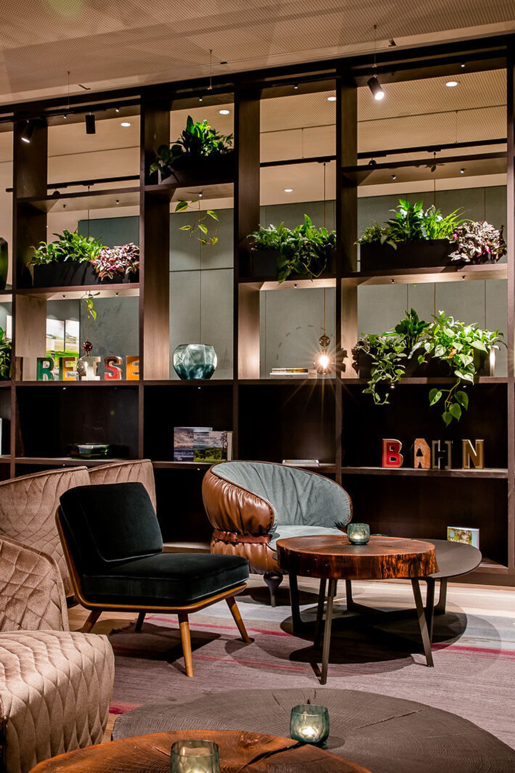 One Lounge mit gemütlichen Sesseln und Sofas in warmen Farben, dekorativen Pflanzen und stilvollen Regalen, die eine entspannte und einladende Atmosphäre schaffen.