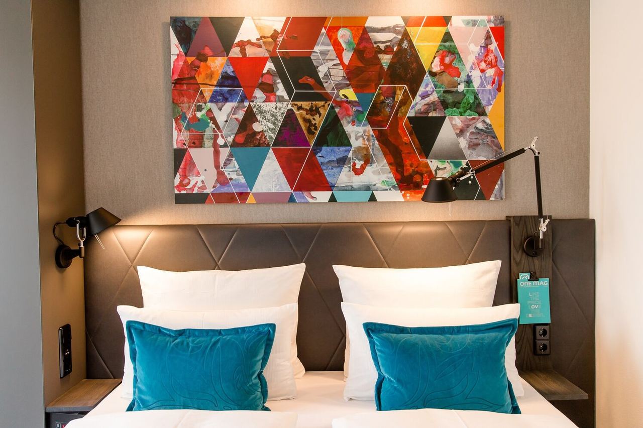 hotel Frankfurt Römer Motel One view of the headboard of a double bed with two decorative cushions and a colorful painting on the wall