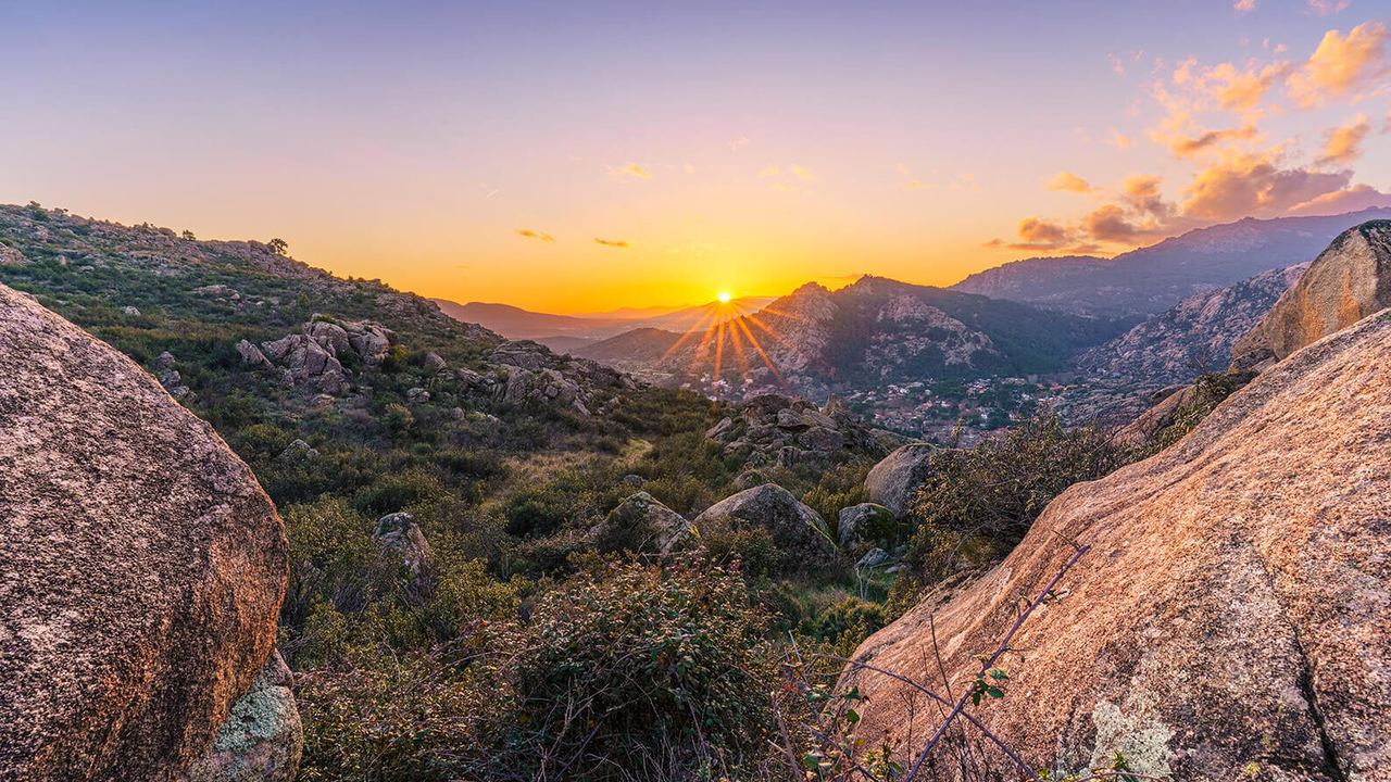 Sonnenuntergang über einer felsigen Berglandschaft mit grüner Vegetation, die Ruhe und natürliche Schönheit ausstrahlt.