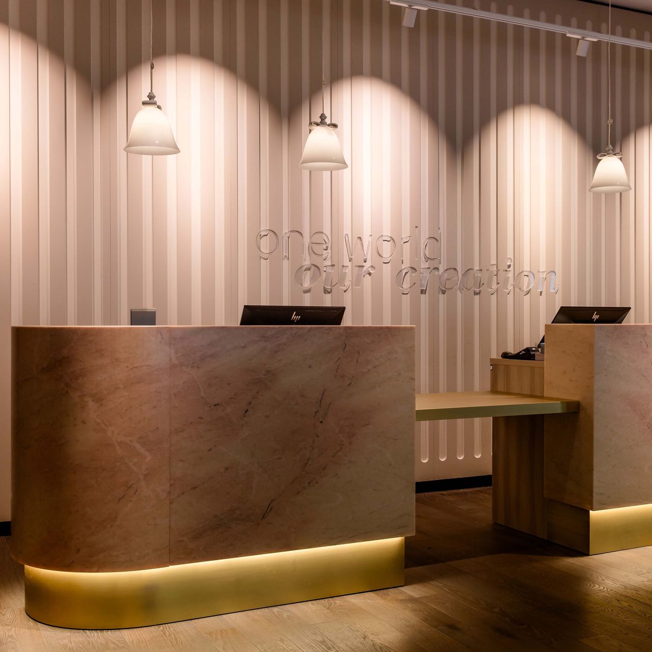 Motel One Rezeption mit elegantem, beleuchtetem Empfangstresen aus Marmor, sanfte Deckenbeleuchtung, Computern und Wänden mit feinem Streifenmuster – einladender Eingangsbereich eines stilvollen Hotels