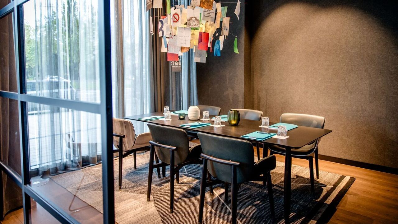Hotel Karlsruhe Motel One Meetingraum mit Tisch, sechs Stühlen sowie bodentiefem Fenster für viel Licht