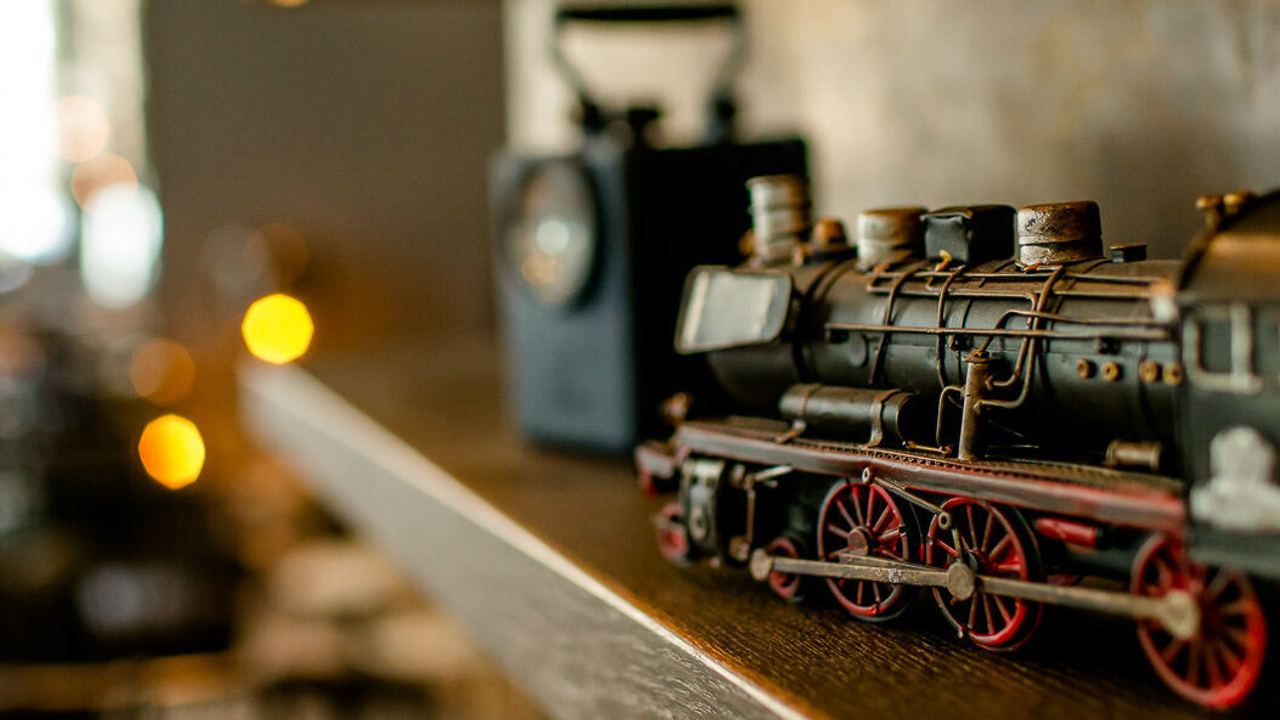 Detailaufnahme einer nostalgischen Modell-Lok aus Metall auf einem Holzregal, umgeben von warmem Licht.