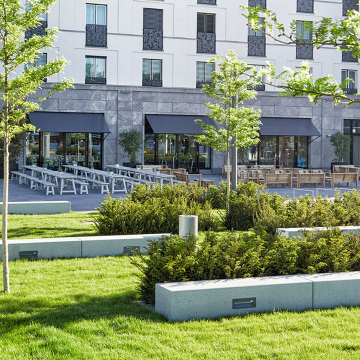 Außenansicht eines modernen Hotels mit Sitzgelegenheiten im Freien und gepflegtem Gartenbereich, der Ruhe und Entspannung in grüner Umgebung bietet.