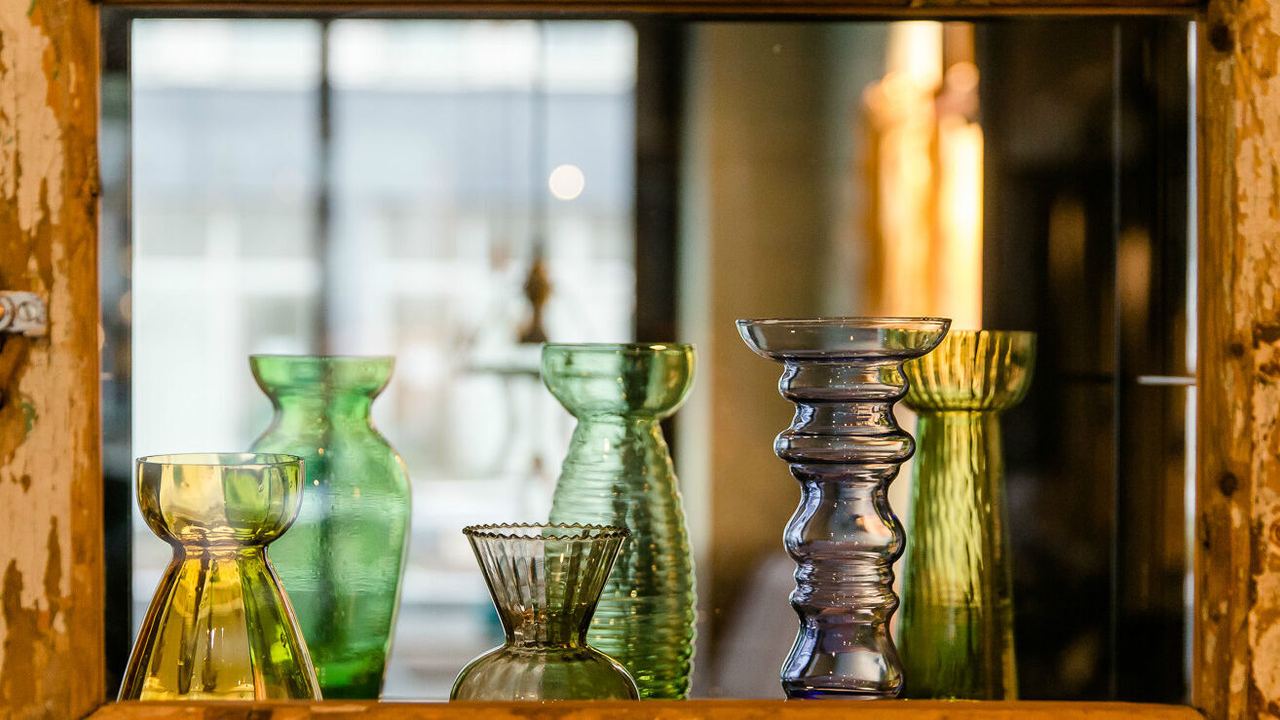 Verschiedene bunte Glasvasen in unterschiedlichen Formen und Größen stehen auf einer rustikalen Holzablage vor einem Spiegel.
