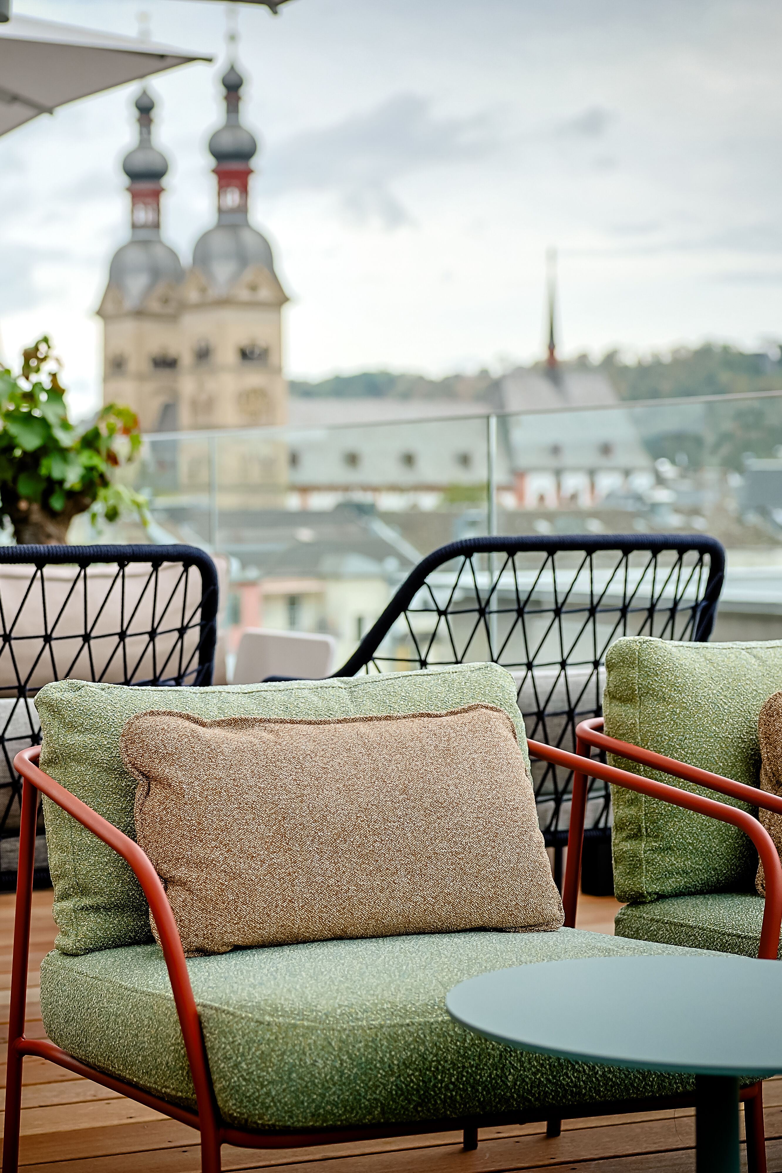 Gemütliche Dachterrassen-Lounge mit gepolsterten Sesseln und Tischen, umgeben von Pflanzen, mit Blick auf historische Kirchtürme in der Stadt. Ideal zum Entspannen und Genießen der Aussicht. Gemütliche Dachterrassen-Lounge mit gepolsterten Sesseln und Tischen, umgeben von Pflanzen, mit Blick auf historische Kirchtürme in der Stadt. Ideal zum Entspannen und Genießen der Aussicht.