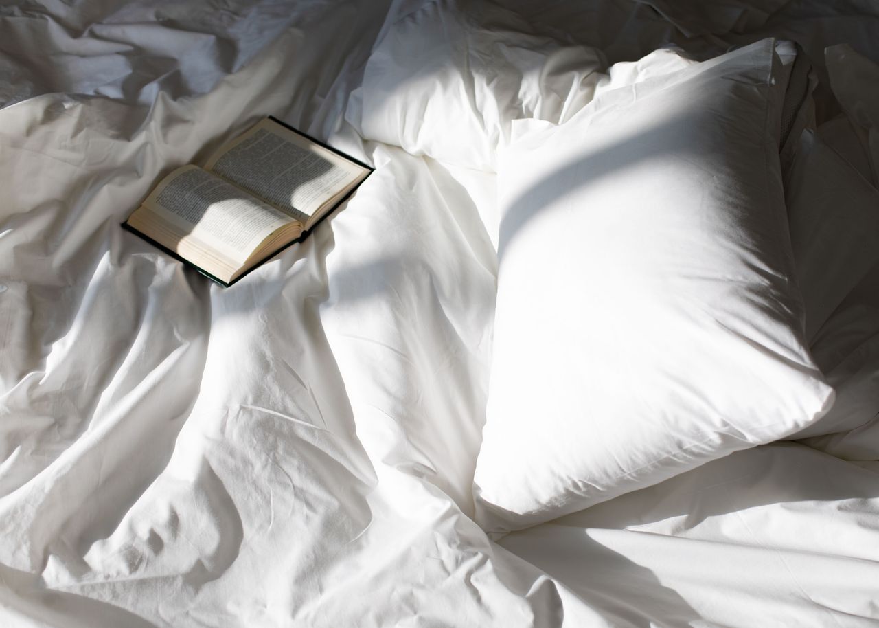 Ein aufgeschlagenes Buch liegt auf den weißen Laken eines Bettes Motel One Hotels