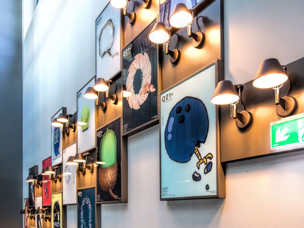 Wandgalerie mit modernen, farbenfrohen Kunstwerken unter warmen Wandlampen.