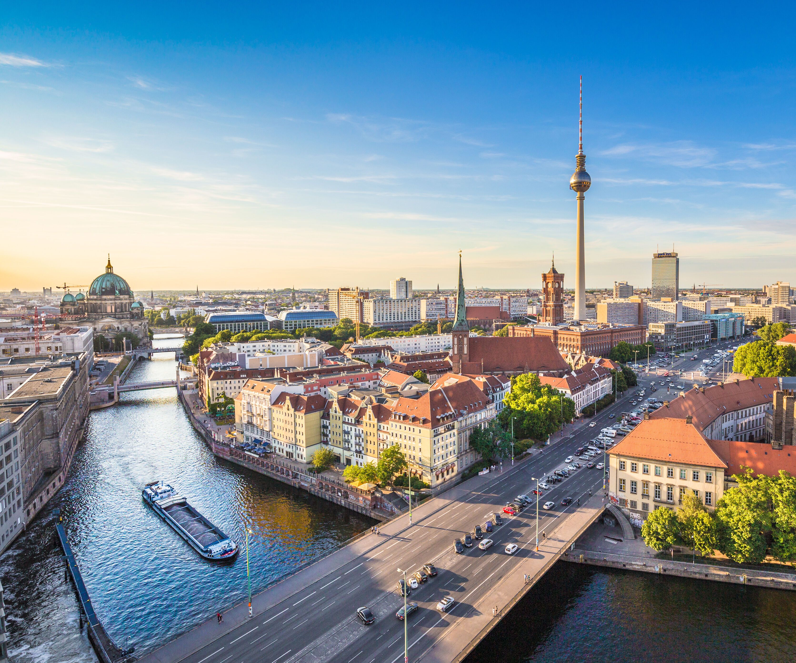 Panoramablick auf Berlins Innenstadt bei Sonnenlicht, mit Blick auf die Spree, historische Gebäude, die Fernsehturm-Silhouette und belebte Straßen. Ideal für Kultur- und Städtereisende.