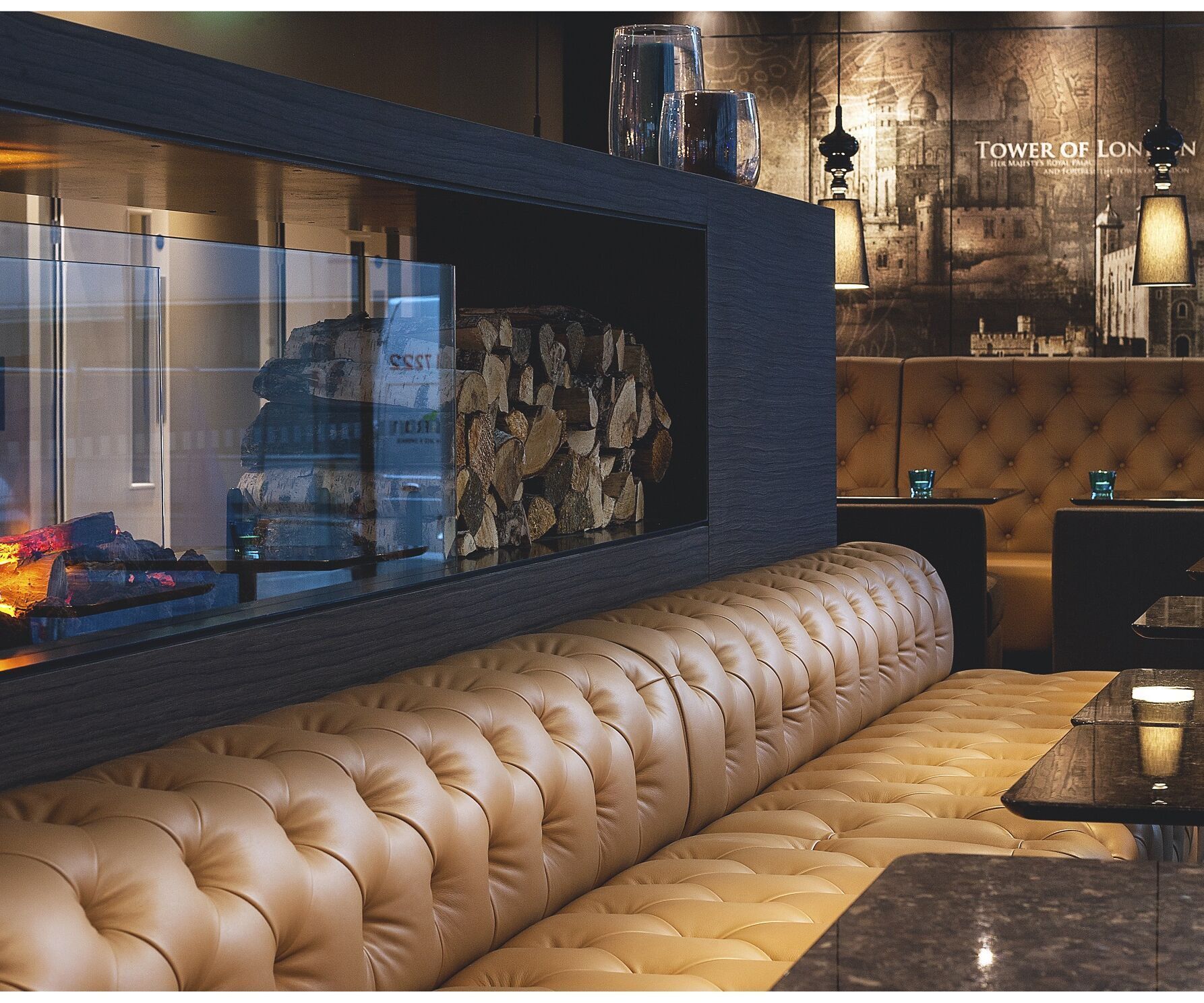 Hotel London Tower Hill Motel One Lounge mit langer Couch sowie Tischen und Kaminfeuer
