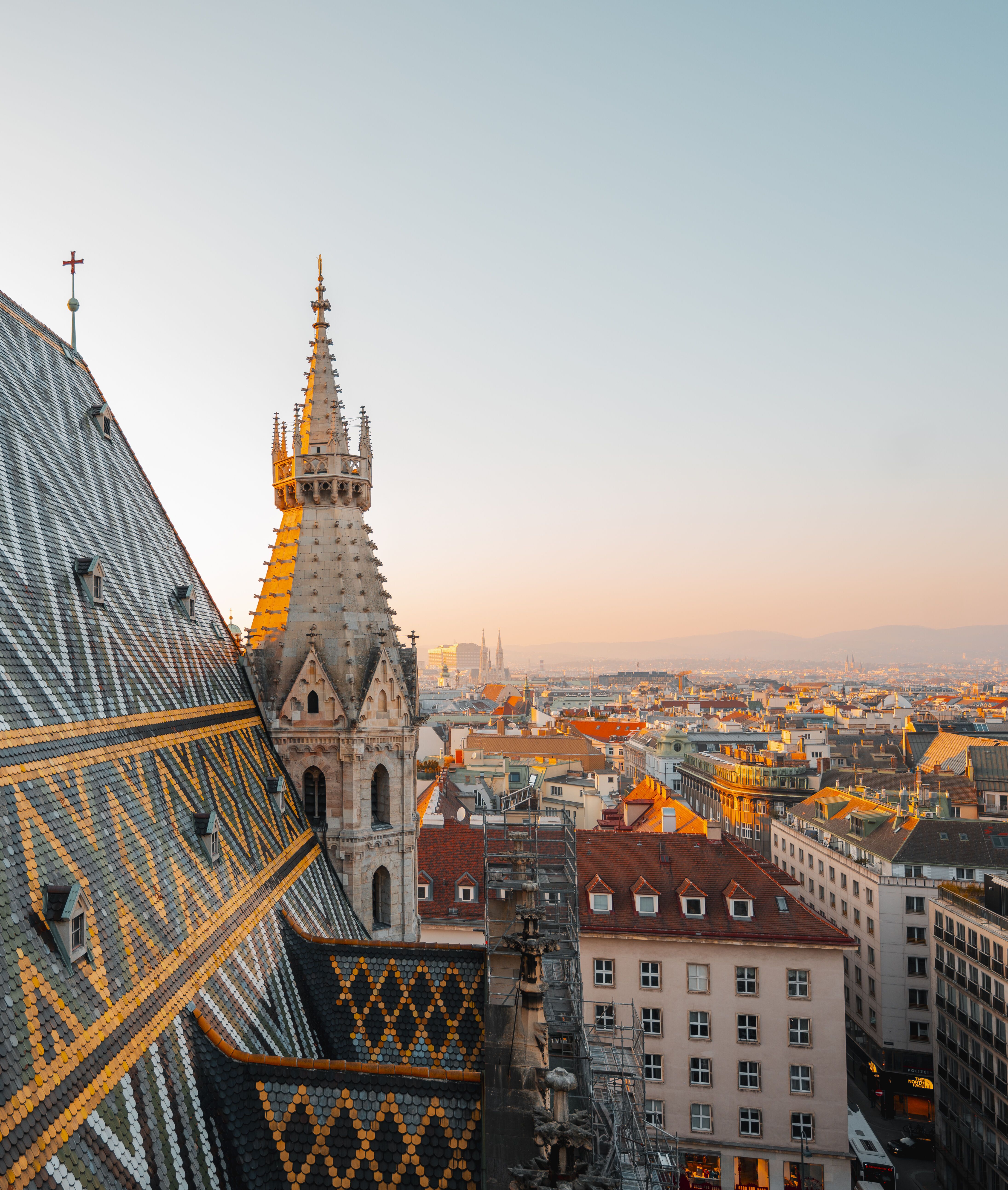 Dach des Stephansdoms in Wien mit bunten Ziegelmustern und Turm im Abendlicht, Blick über die Stadt mit historischen Gebäuden und sanftem Himmel.