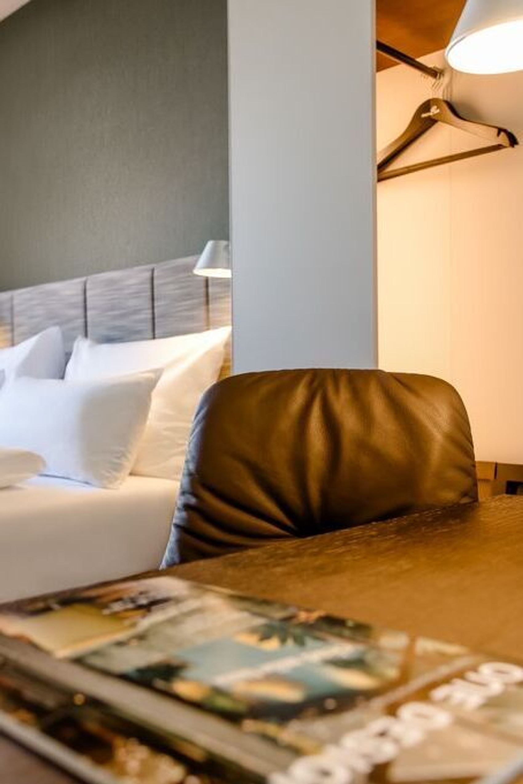 Helles Hotelzimmer mit gemütlichem Doppelbett, dunklen Vorhängen und Schreibtisch mit Leselampe und Stuhl.
