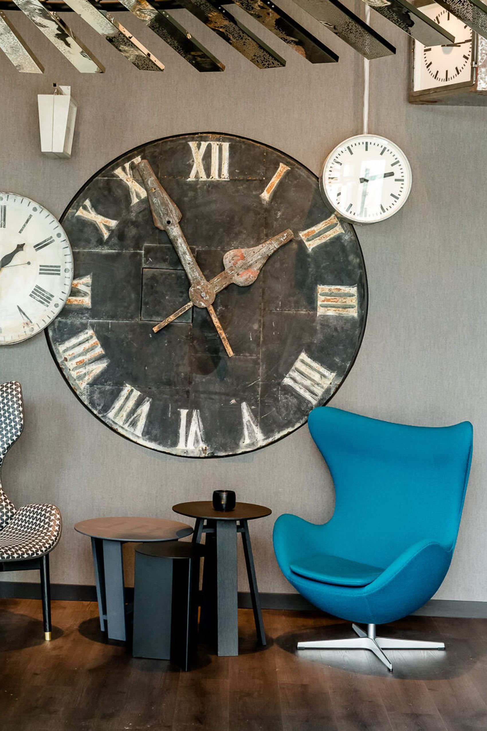 designhotel Berlin Hauptbahnhof Motel One view of a chair and an egg chair with side tables in between, as well as several clocks on the wall