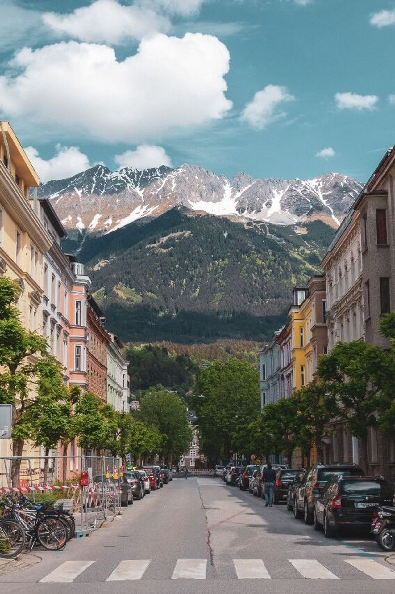 Hotel Innsbruck Motel One breite Straße mit Häusern links und rechts und mittiger Blick auf die Berge
