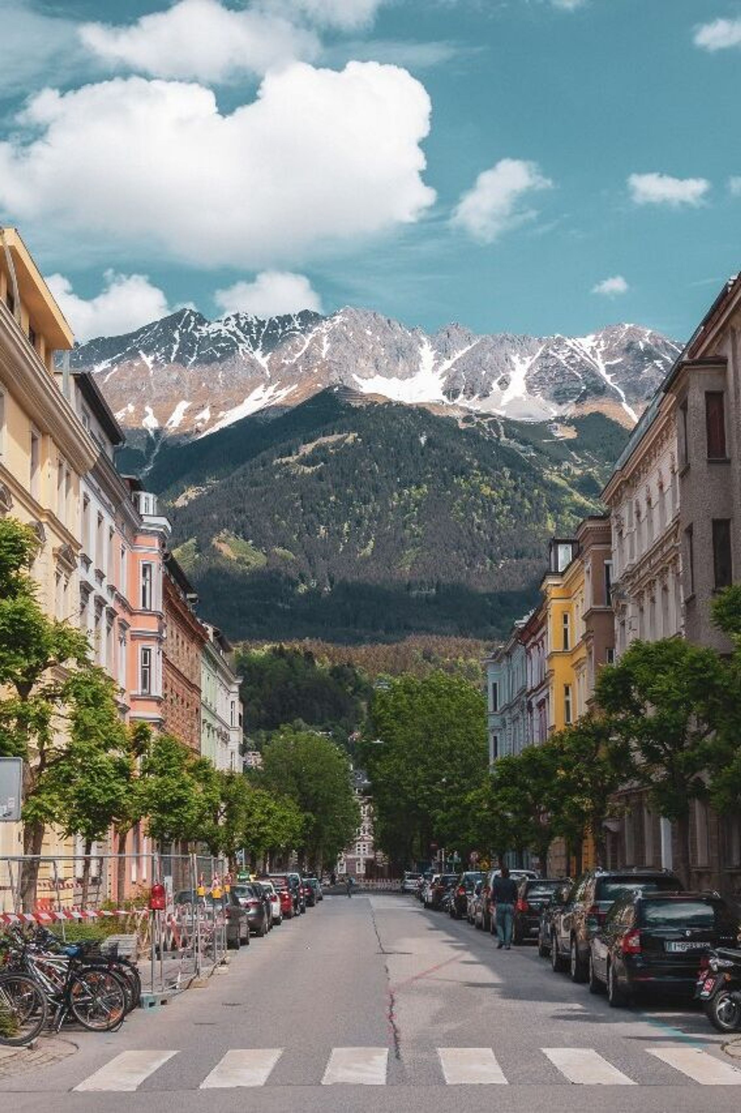 Hotel Innsbruck Motel One breite Straße mit Häusern links und rechts und mittiger Blick auf die Berge