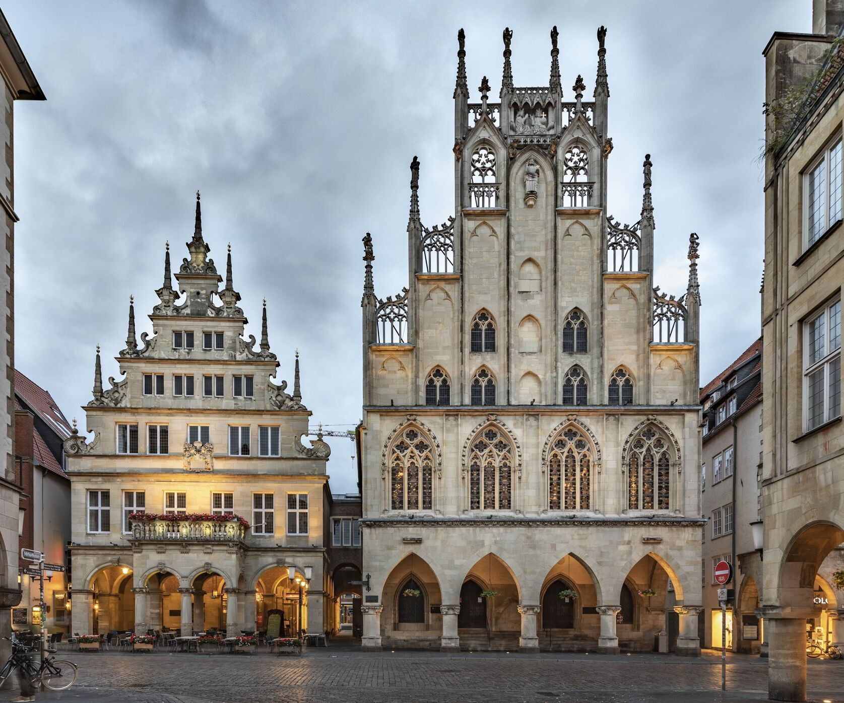 Blick auf das historische Rathaus mit gotischer Fassade und dem angrenzenden Renaissance-Gebäude am belebten Marktplatz, umgeben von weiteren historischen Gebäuden unter bewölktem Himmel.