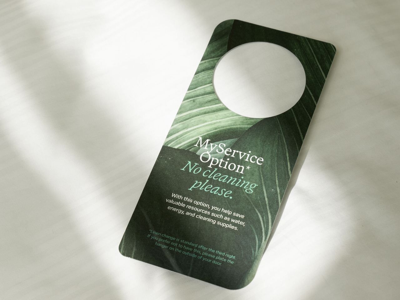 Türanhänger auf weißer Bettwäsche mit der Aufschrift „My service option – No cleaning please“, der anzeigt, dass keine Zimmerreinigung gewünscht ist. Türanhänger auf weißer Bettwäsche mit der Aufschrift „My service option – No cleaning please“, der anzeigt, dass keine Zimmerreinigung gewünscht ist.