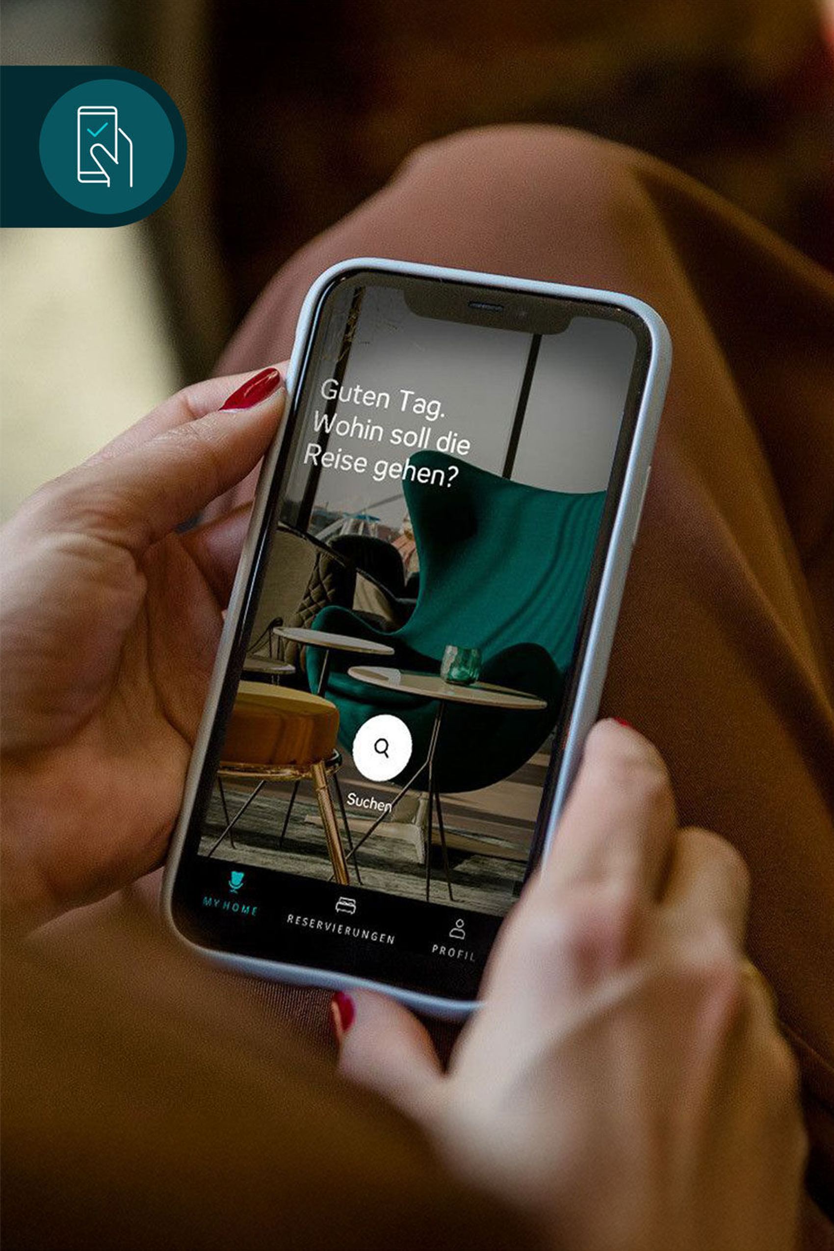 Person hält Smartphone mit einer Reisebuchungs-App, auf dem Bildschirm steht: „Guten Tag. Wohin soll die Reise gehen?“. Im Hintergrund sind stilvolle Stühle und ein Tisch zu sehen.