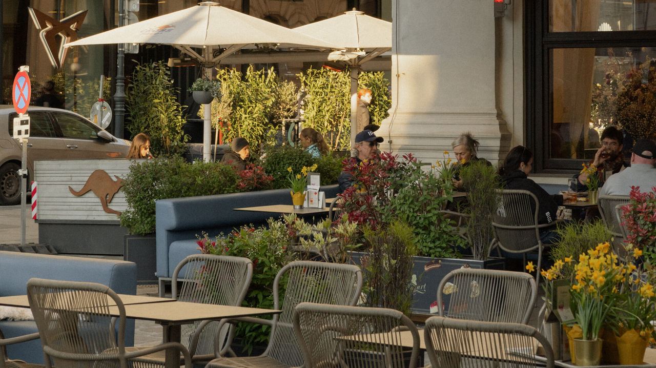 Außenbereich eines Cafés mit Sonnenschirmen und Sitzgelegenheiten, Menschen genießen bei warmem Licht Speisen und Getränke in entspannter Atmosphäre. Außenbereich eines Cafés mit Sonnenschirmen und Sitzgelegenheiten, Menschen genießen bei warmem Licht Speisen und Getränke in entspannter Atmosphäre.