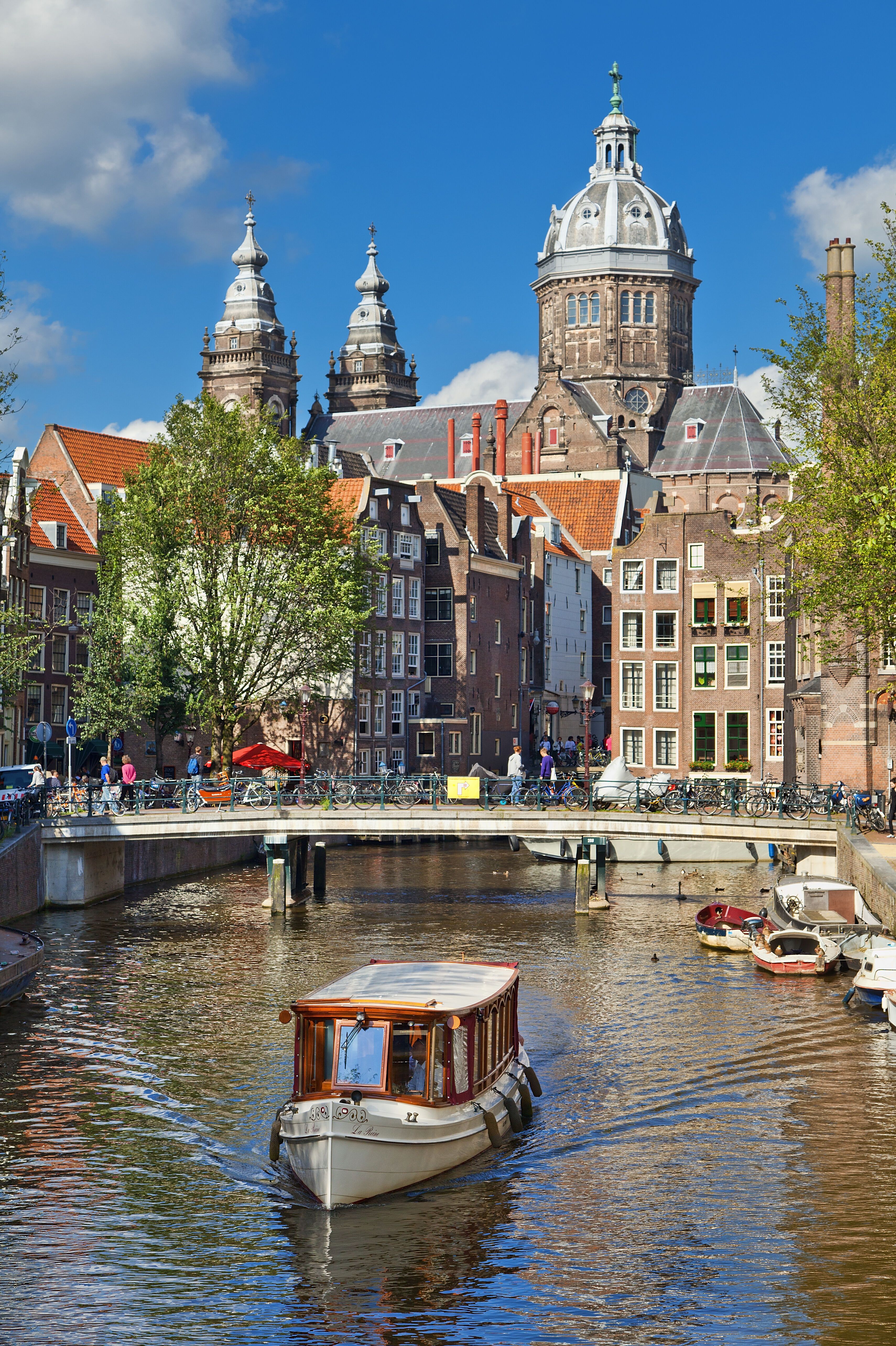 Blick auf einen historischen Stadtkanal mit einem kleinen Bootsfahrgastschiff, umgeben von klassischen Gebäuden und Türmen unter blauem Himmel, typisch für eine europäische Stadt mit reicher Architektur und Wasserwegen.