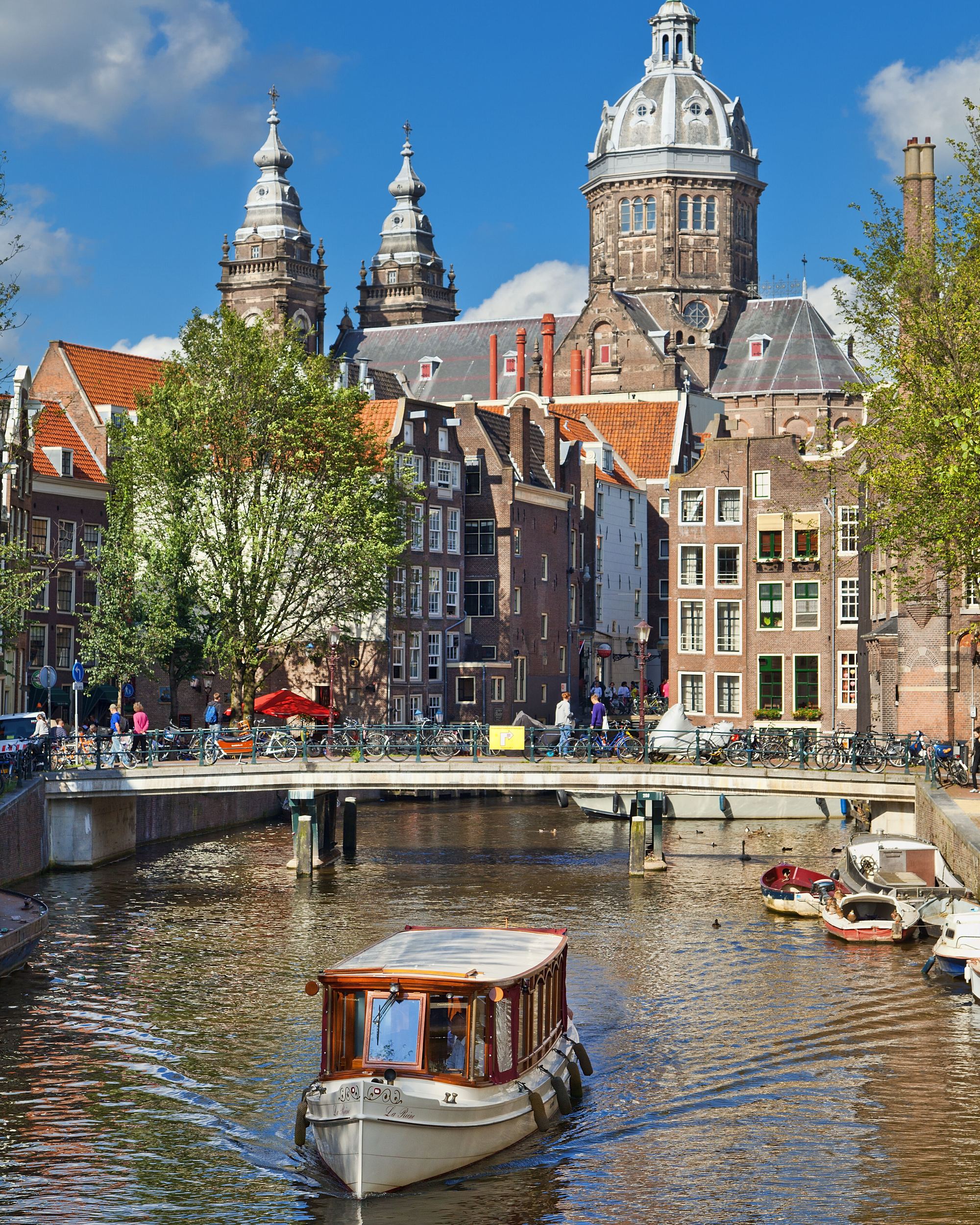 Blick auf einen historischen Stadtkanal mit einem kleinen Bootsfahrgastschiff, umgeben von klassischen Gebäuden und Türmen unter blauem Himmel, typisch für eine europäische Stadt mit reicher Architektur und Wasserwegen.