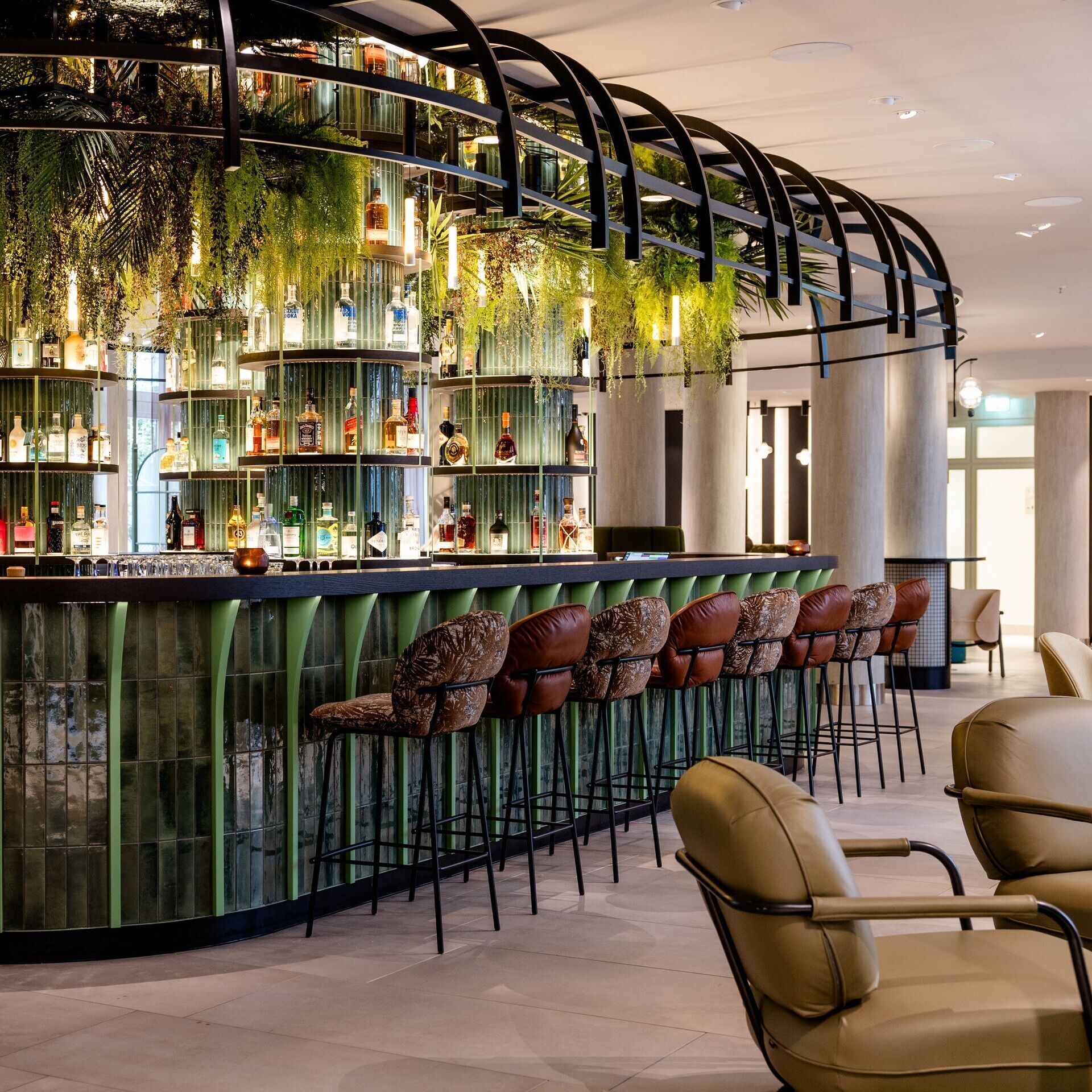 Hotel Frankfurt-Hauptbahnhof Motel One bar with green glass counter, high bar stools and hanging plants, creating a relaxed and stylish atmosphere.
