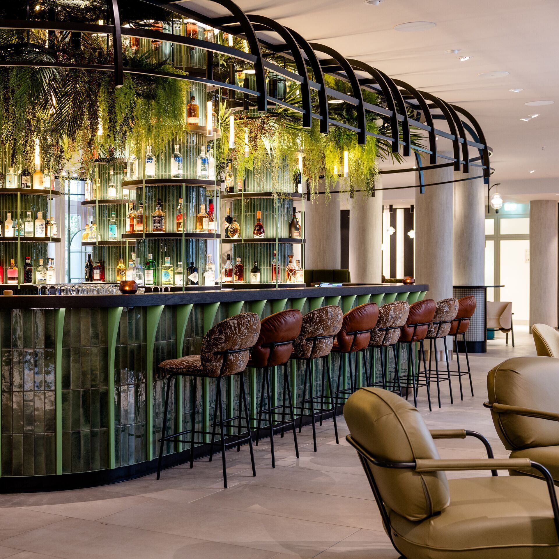 Hotel Frankfurt-Hauptbahnhof Motel One bar with green glass counter, high bar stools and hanging plants, creating a relaxed and stylish atmosphere.