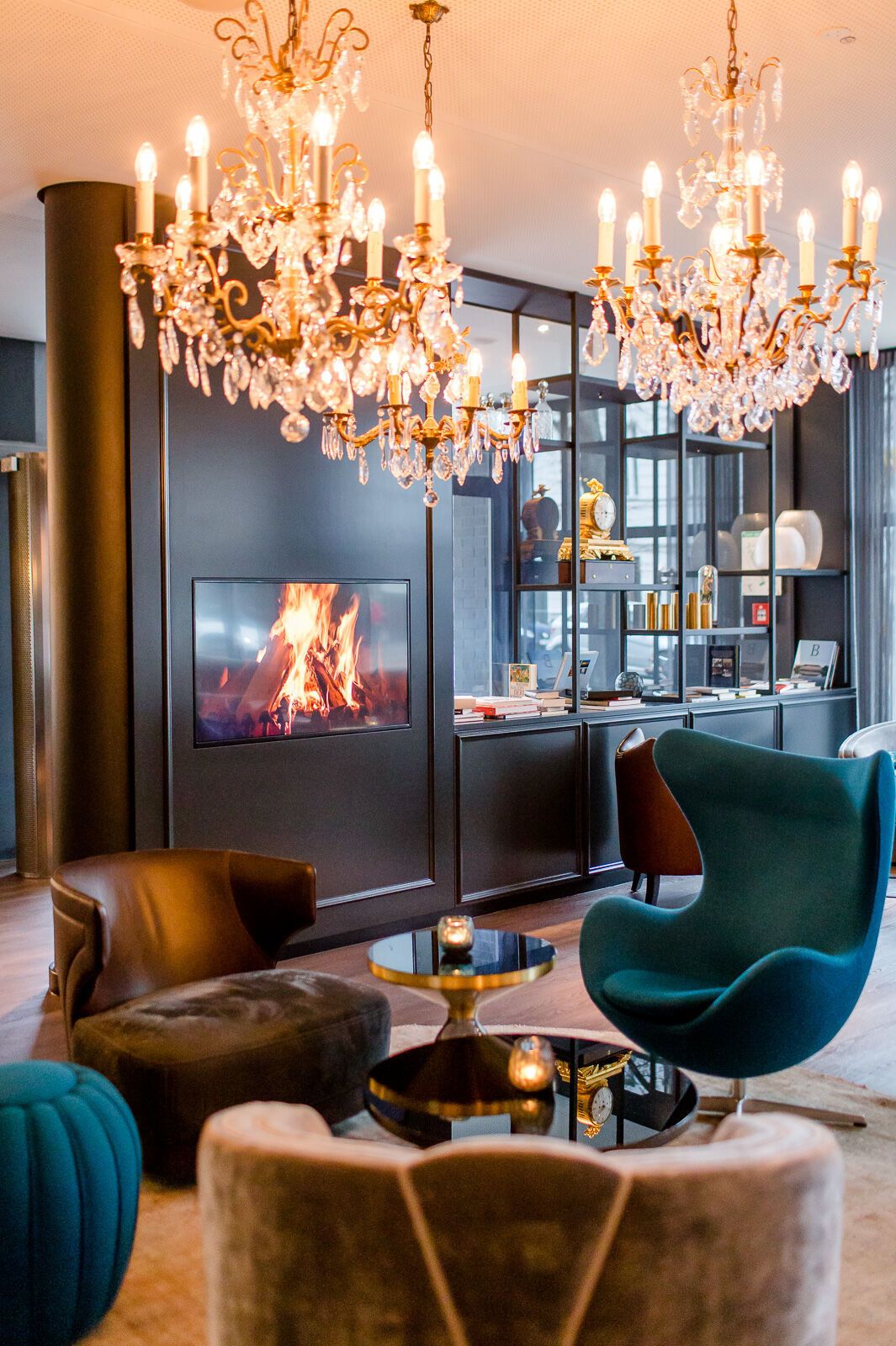hotel Berlin Bellevue Motel One light-filled lounge with armchairs, egg chair, wall-mounted TV, chandelier on the ceiling, and open shelving in the background