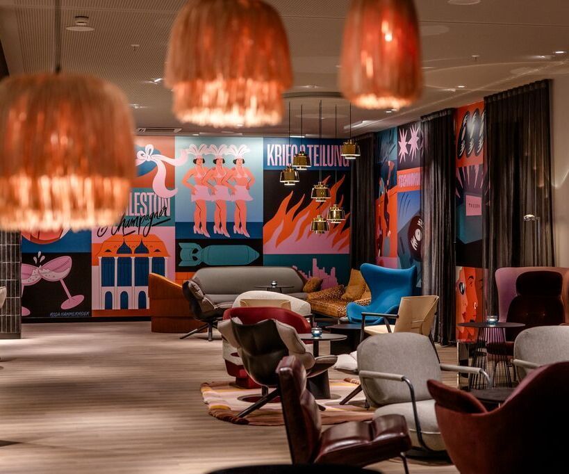 Gemütlicher Lounge-Bereich mit modernen Sesseln, warmem Licht und farbenfrohen, kunstvollen Wandbildern, der eine entspannte Atmosphäre zum Verweilen schafft.