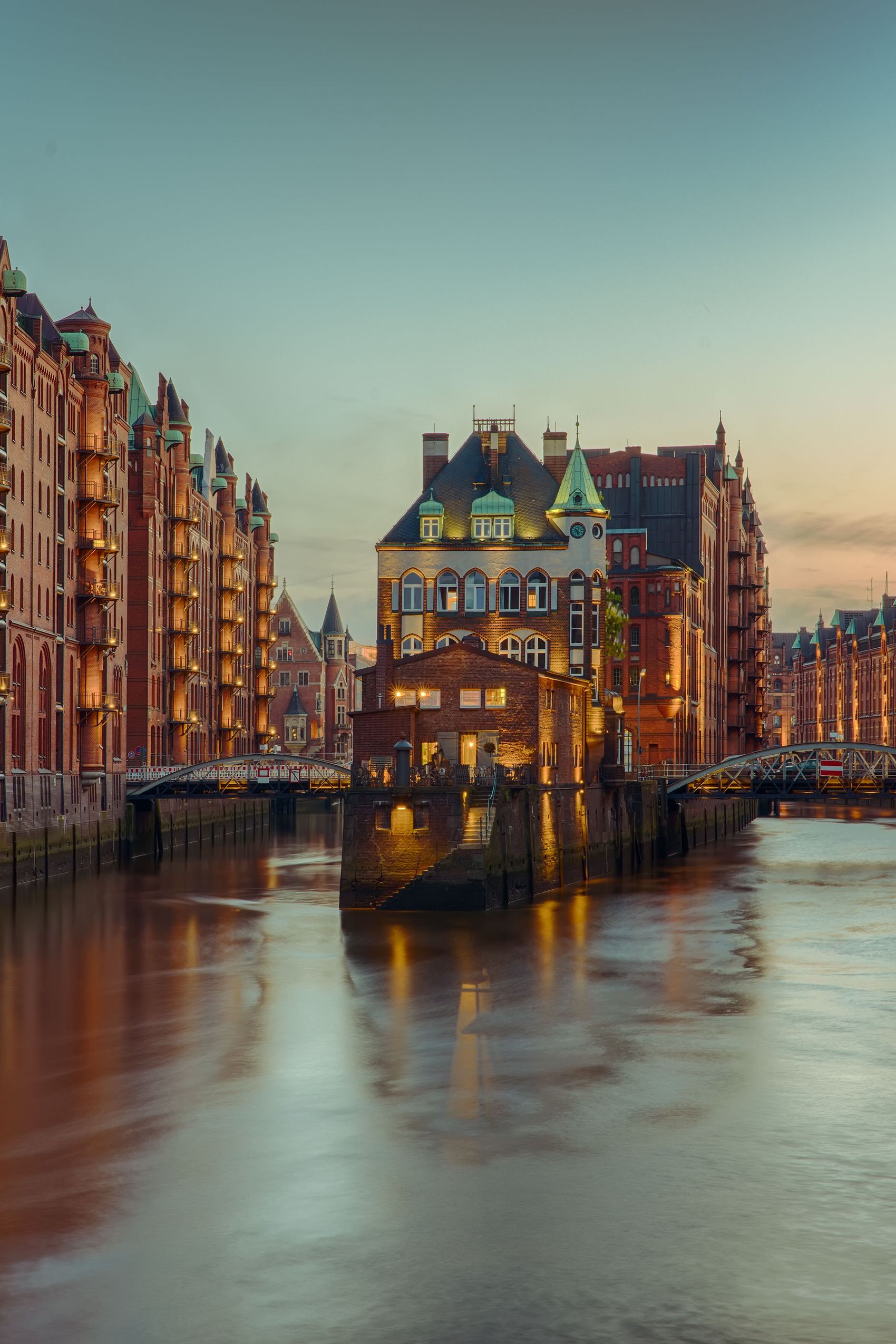 Blick auf einen historischen Wasserkanal in der Dämmerung, umgeben von beleuchteten, roten Backsteingebäuden mit Balkonen, die eine warme Atmosphäre und urbanen Charme vermitteln.