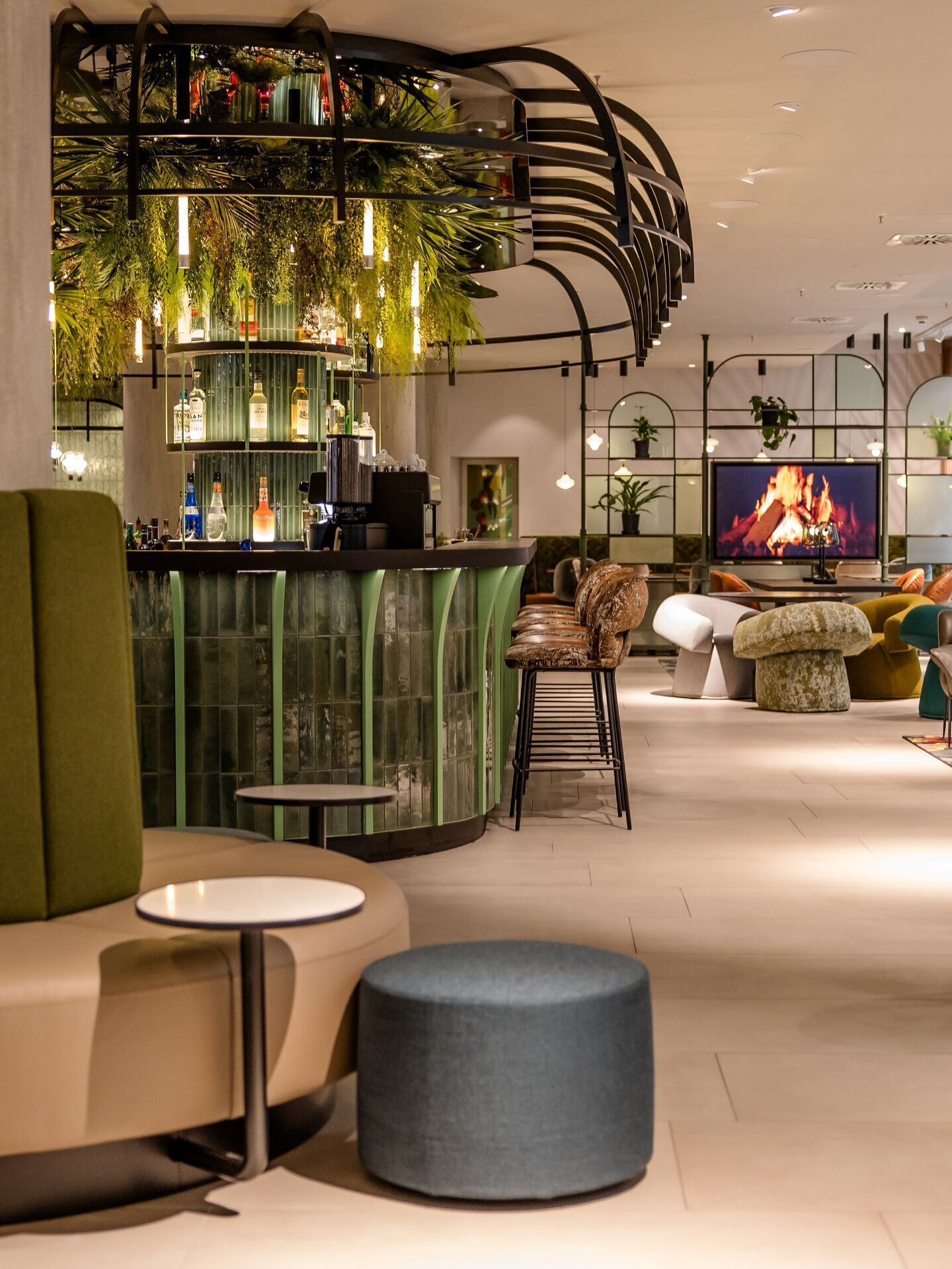 Hotel Frankfurt-Hauptbahnhof Motel One helle Lounge mit gemütlichen Sitzgelegenheiten, Bar, Pflanzen-Dekor und einem digitalen Kamin.