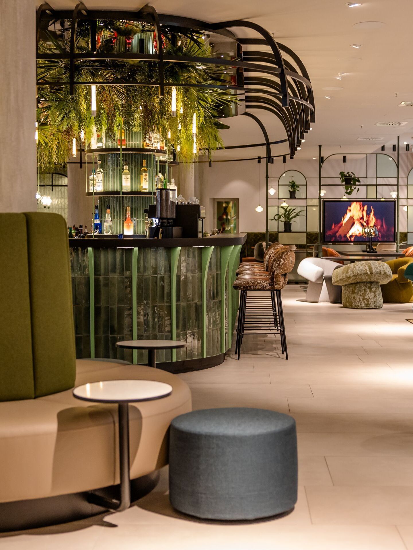 Hotel Frankfurt-Hauptbahnhof Motel One helle Lounge mit gemütlichen Sitzgelegenheiten, Bar, Pflanzen-Dekor und einem digitalen Kamin.