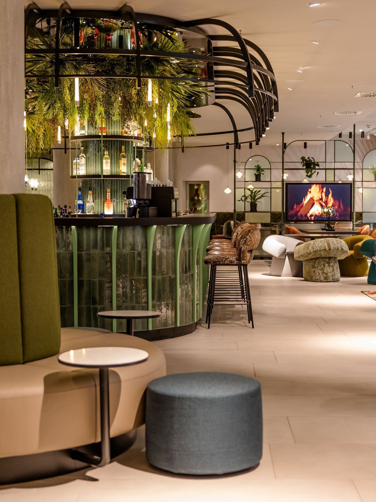 Hotel Frankfurt-Hauptbahnhof Motel One helle Lounge mit gemütlichen Sitzgelegenheiten, Bar, Pflanzen-Dekor und einem digitalen Kamin.