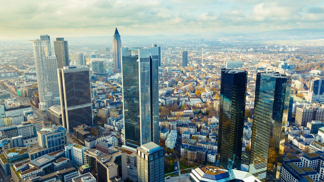 Blick auf die Skyline von Frankfurt mit Hotels Frankfurt und zahlreichen Wolkenkratzern, die in der Morgensonne glänzen, und einem weitläufigen Stadtgebiet im Hintergrund.
