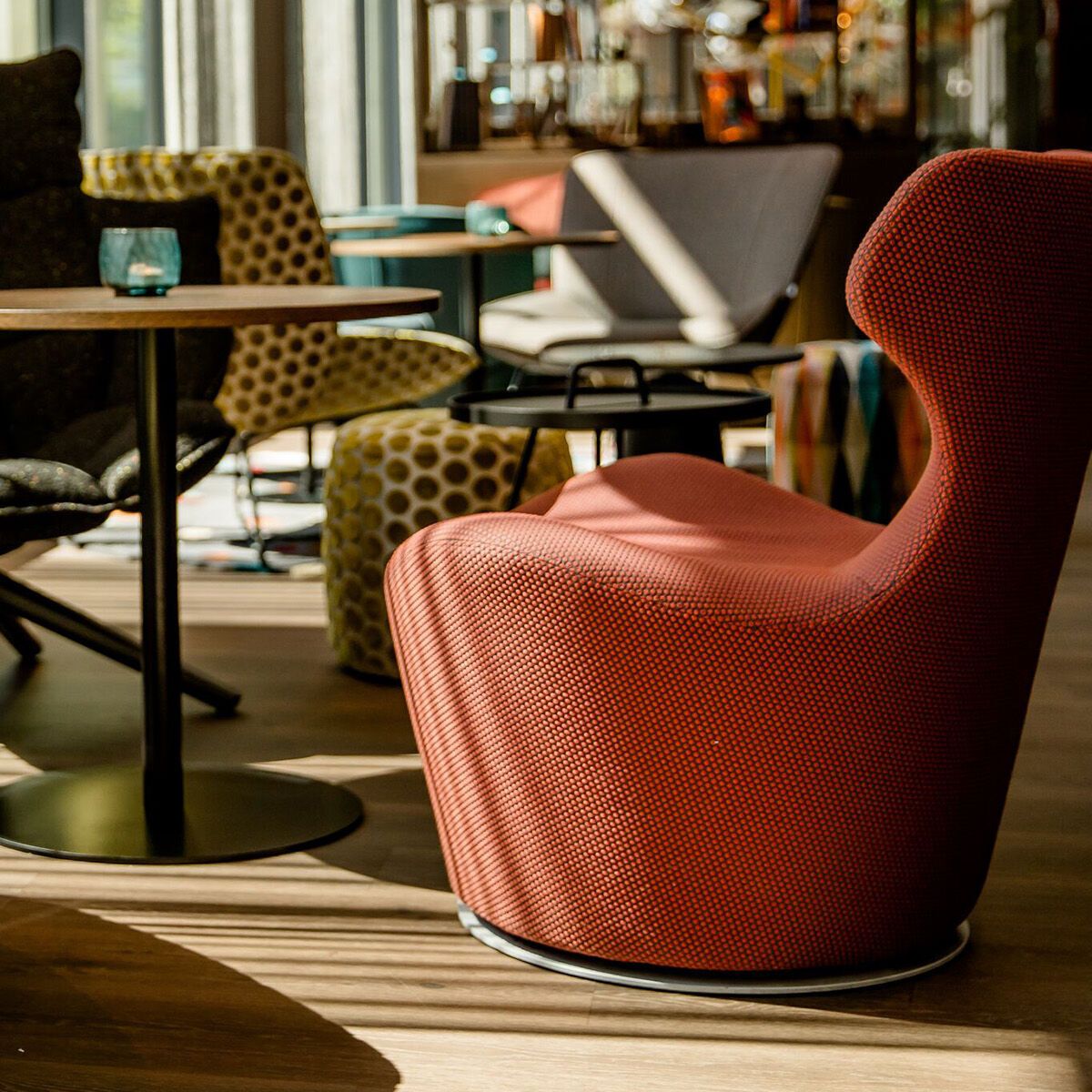 Helle, stilvoll eingerichtete Lounge mit bunten Sesseln, kleinen Tischen und großen Fenstern, die viel Tageslicht hereinlassen. Moderne Atmosphäre zum Entspannen oder für Gespräche.