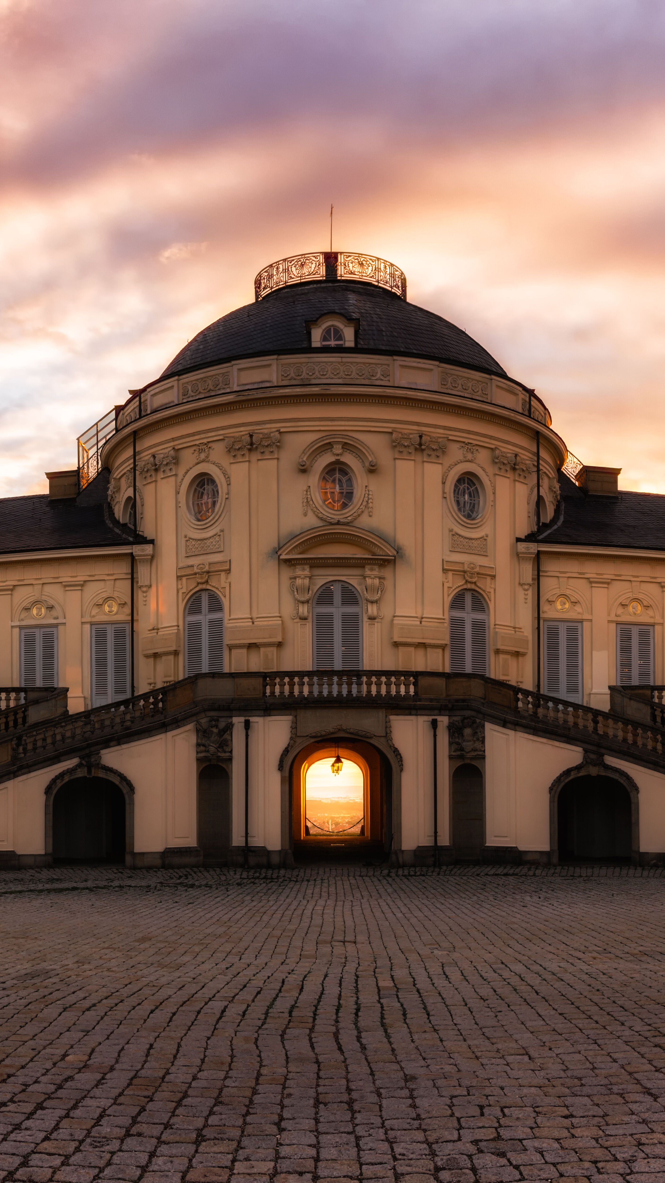 Barockes Schloss mit symmetrischen Treppen, im Sonnenuntergang hell erleuchtet, vermittelt historische Eleganz und ruhige Atmosphäre.