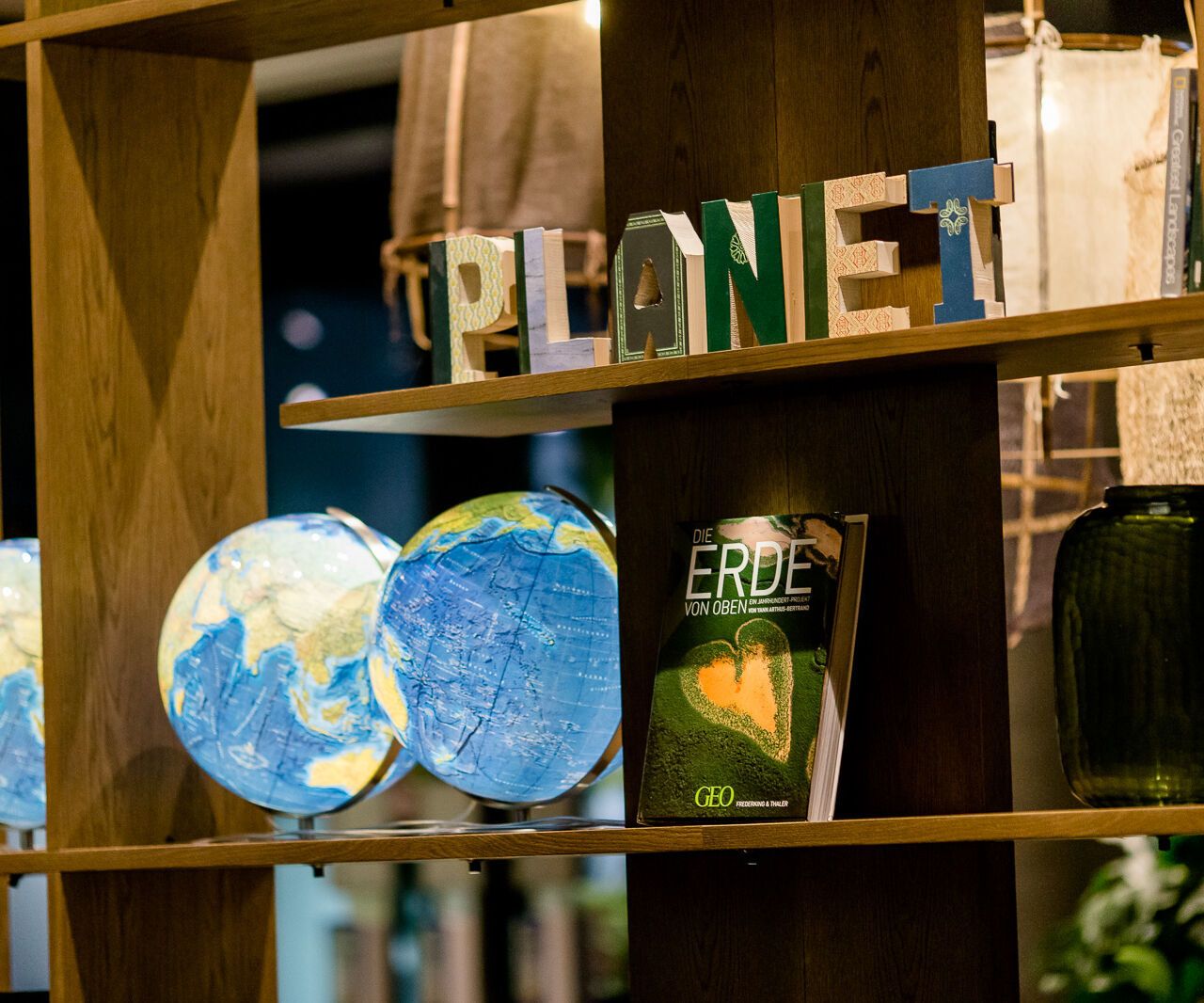 Regal mit drei Weltkugeln, einem Buch über die Erde und Buchstaben, die das Wort „PLANET“ bilden; dekorative Darstellung zur Förderung von Umweltbewusstsein.