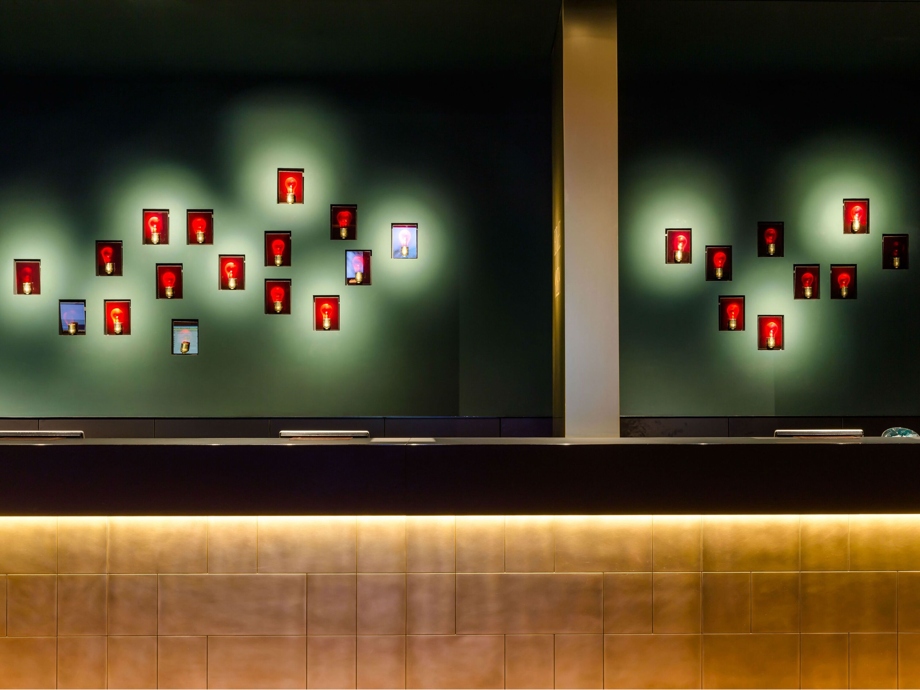 Moderne Hotelrezeption mit stilvoller Wandbeleuchtung und dekorativen, rot hinterleuchteten Bildern, die eine warme und einladende Atmosphäre schaffen.