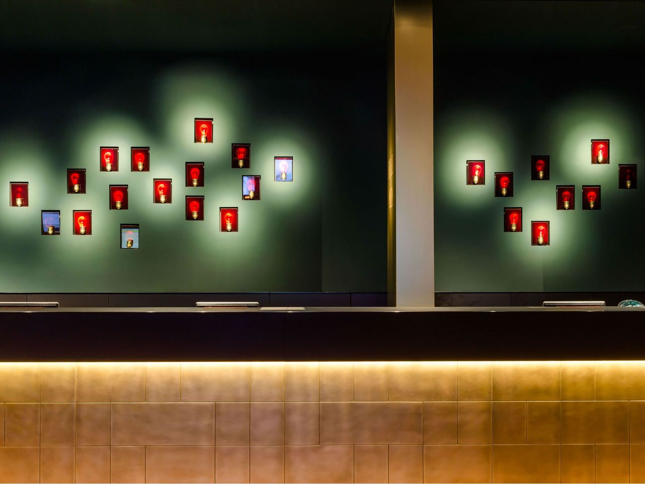 Moderne Hotelrezeption mit stilvoller Wandbeleuchtung und dekorativen, rot hinterleuchteten Bildern, die eine warme und einladende Atmosphäre schaffen.