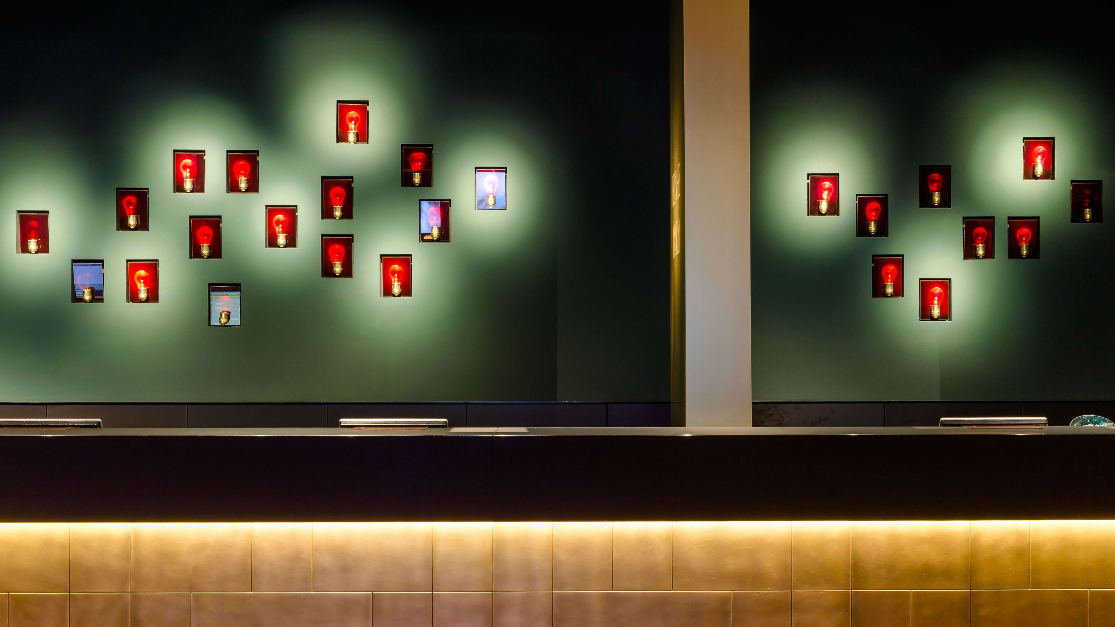 Moderne Hotelrezeption mit stilvoller Wandbeleuchtung und dekorativen, rot hinterleuchteten Bildern, die eine warme und einladende Atmosphäre schaffen.