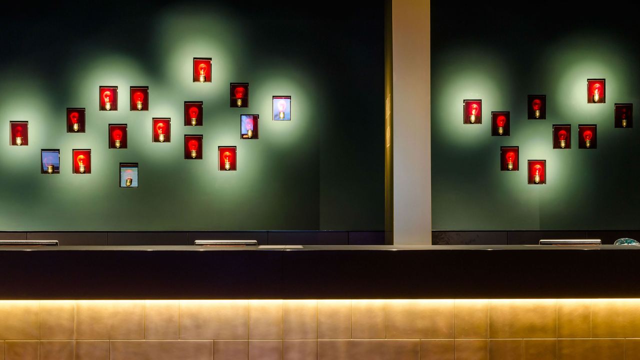 Moderne Hotelrezeption mit stilvoller Wandbeleuchtung und dekorativen, rot hinterleuchteten Bildern, die eine warme und einladende Atmosphäre schaffen.