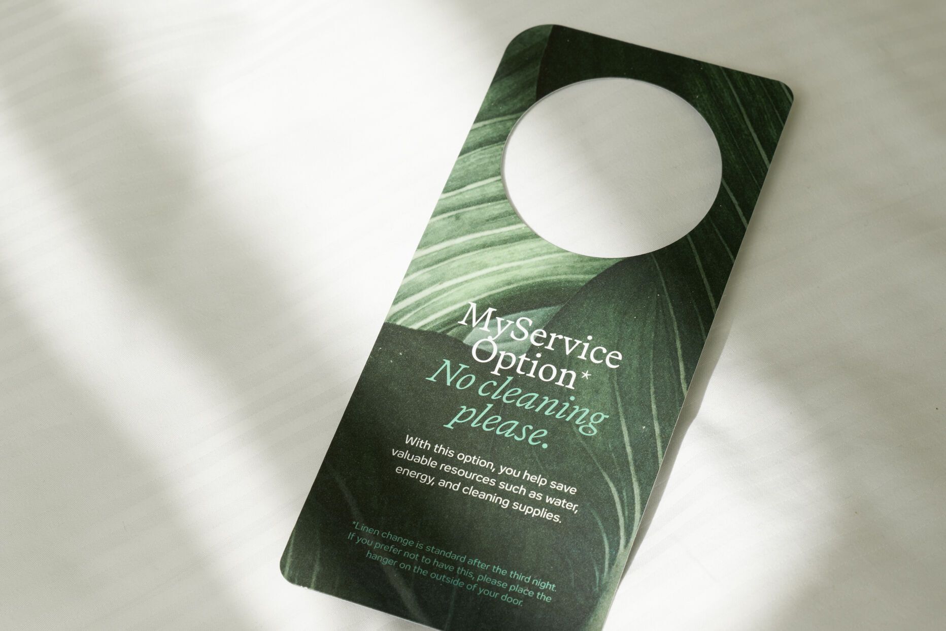 Türanhänger auf weißer Bettwäsche mit der Aufschrift „My service option – No cleaning please“, der anzeigt, dass keine Zimmerreinigung gewünscht ist.