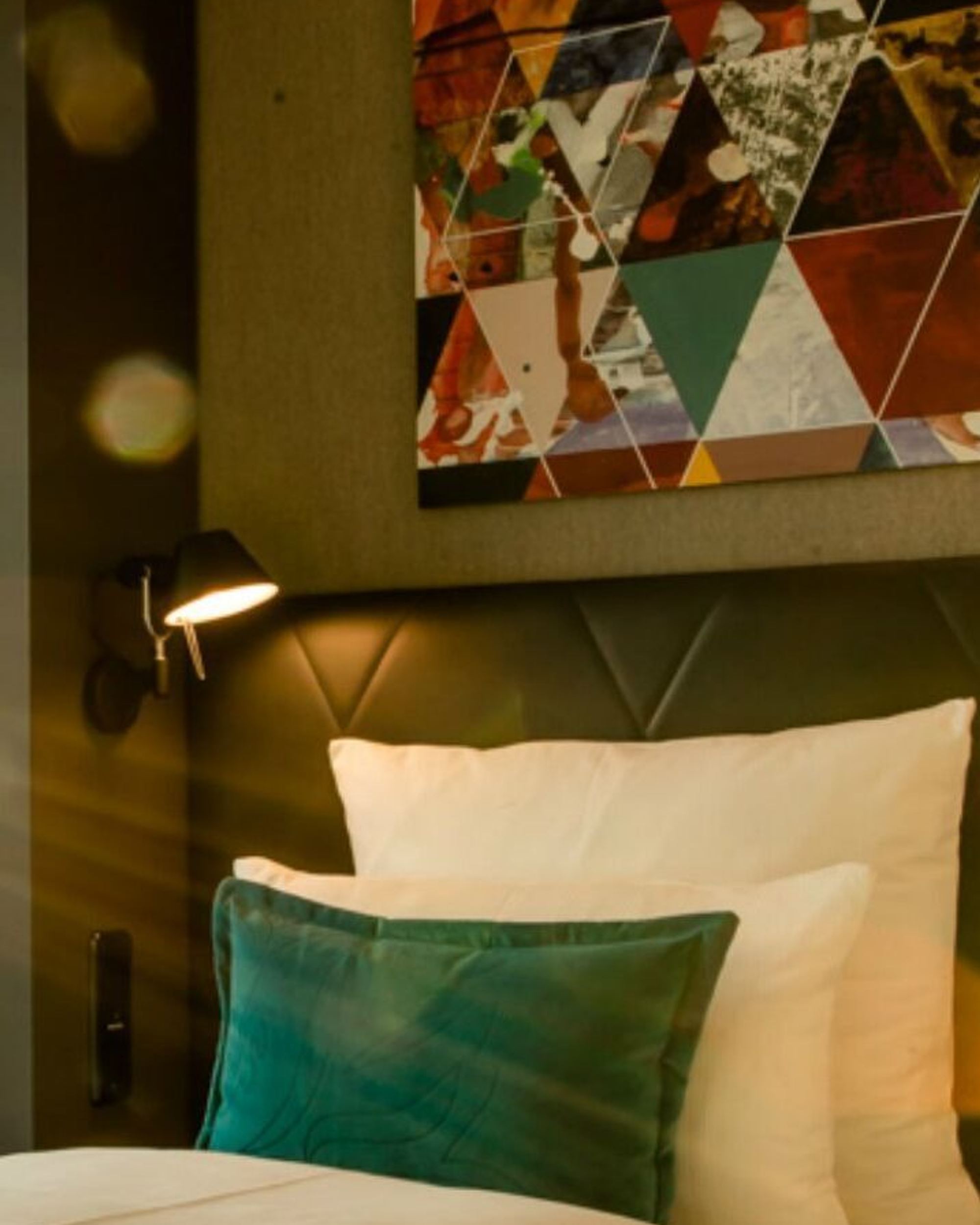 Helles Hotelzimmer mit großen Fenstern, zwei Betten mit weißen Laken und türkisfarbenen Kissen Beleuchtung und stilvoller Wanddekoration. Sonnenlicht strahlt warm herein.